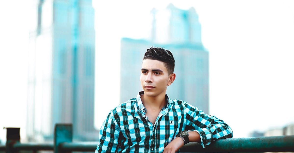 A young man in a plaid shirt is leaning on a railing.