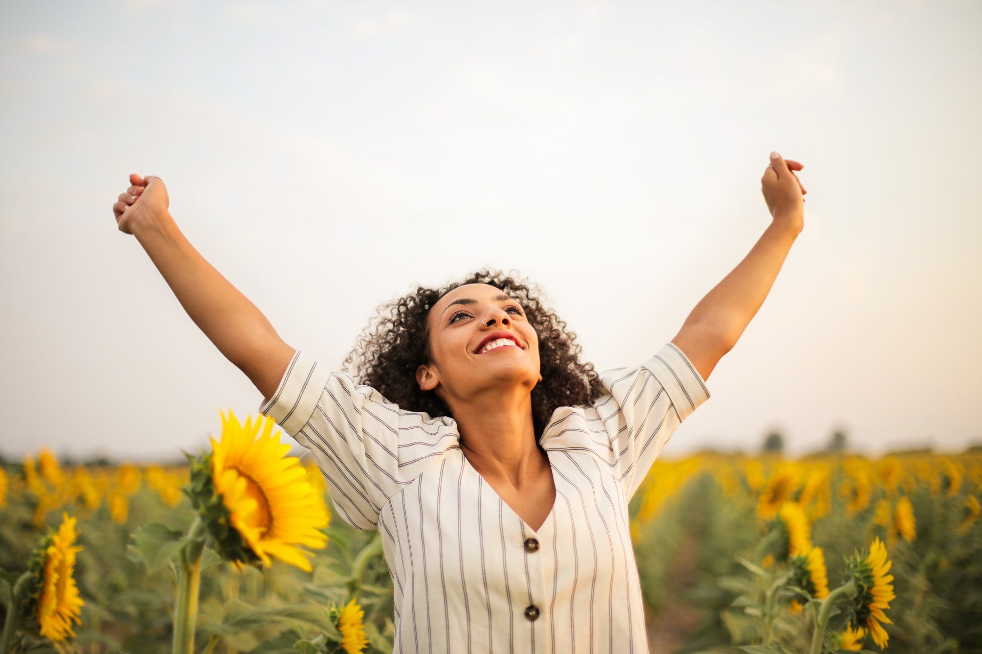 A woman is standing in a field of sunflowers with her arms outstretched.
