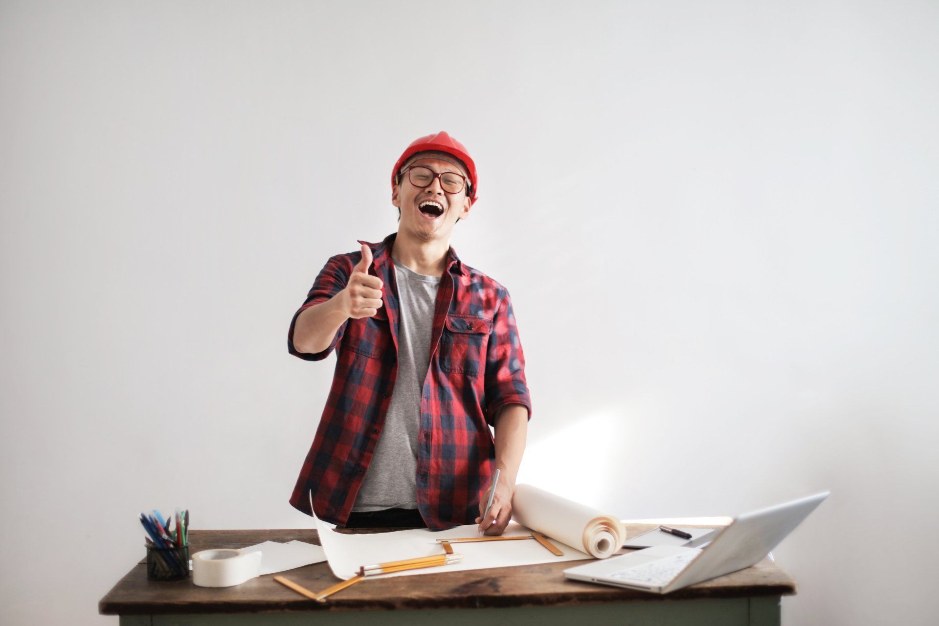 A man is standing at a desk with a laptop and giving a thumbs up.