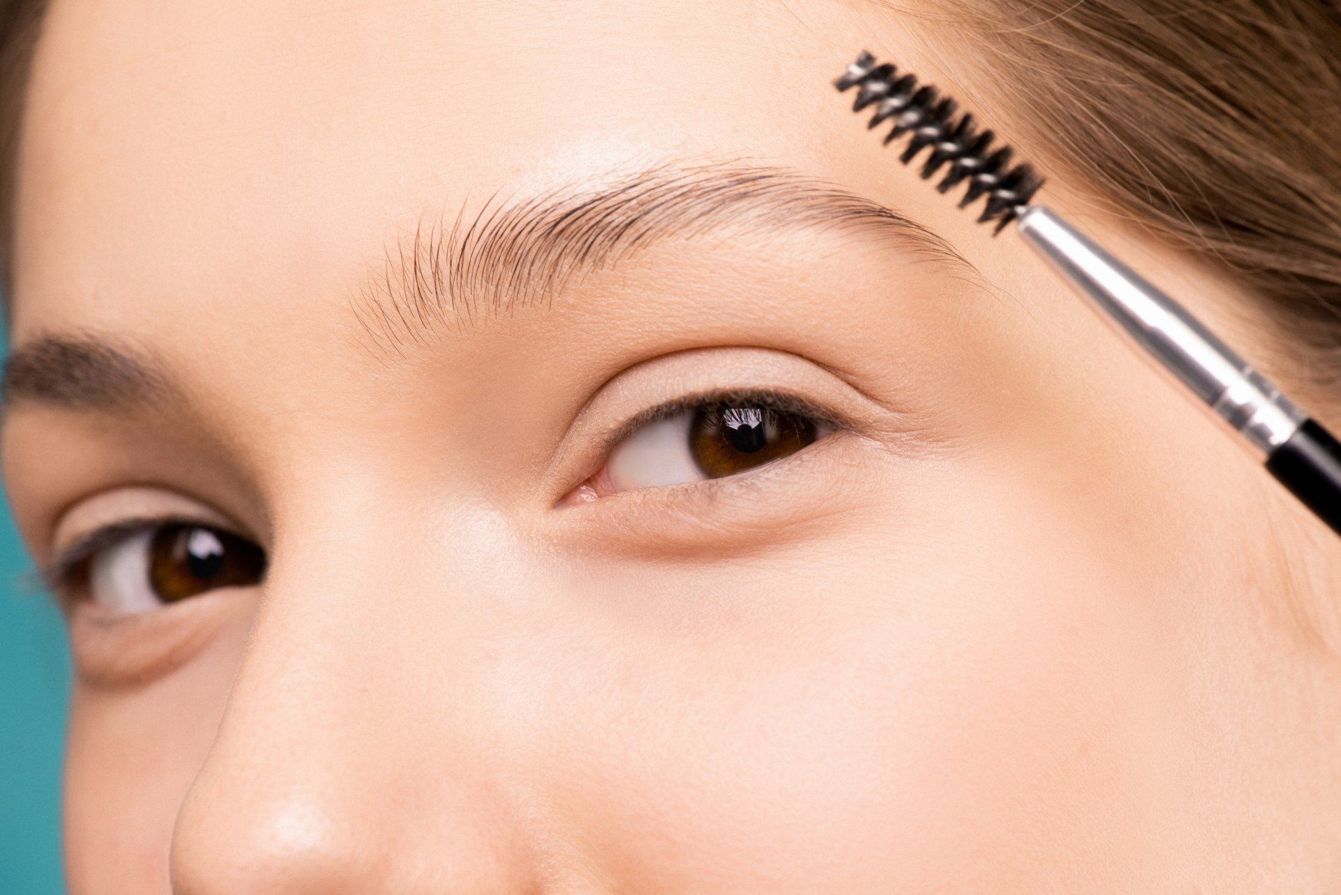 A woman is brushing her eyebrows with a brush.