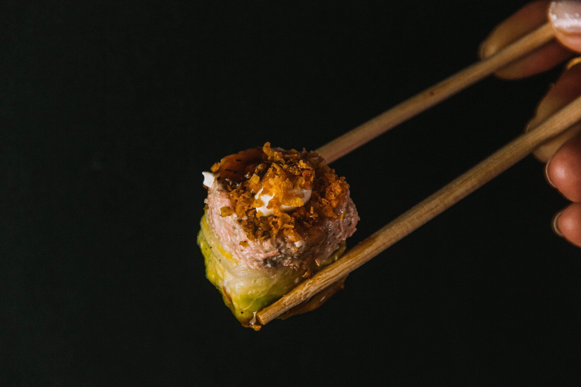 A person is holding a piece of sushi with chopsticks.