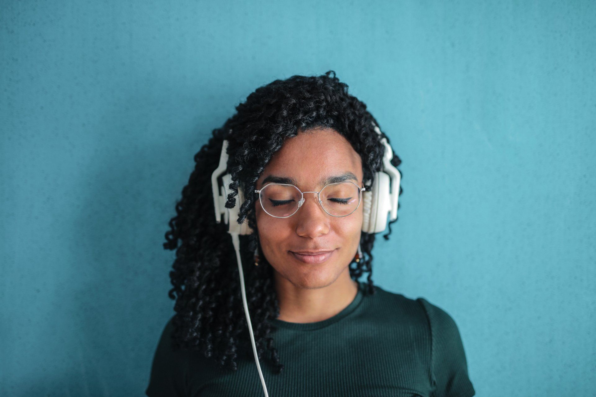 A woman wearing headphones and glasses is listening to music.