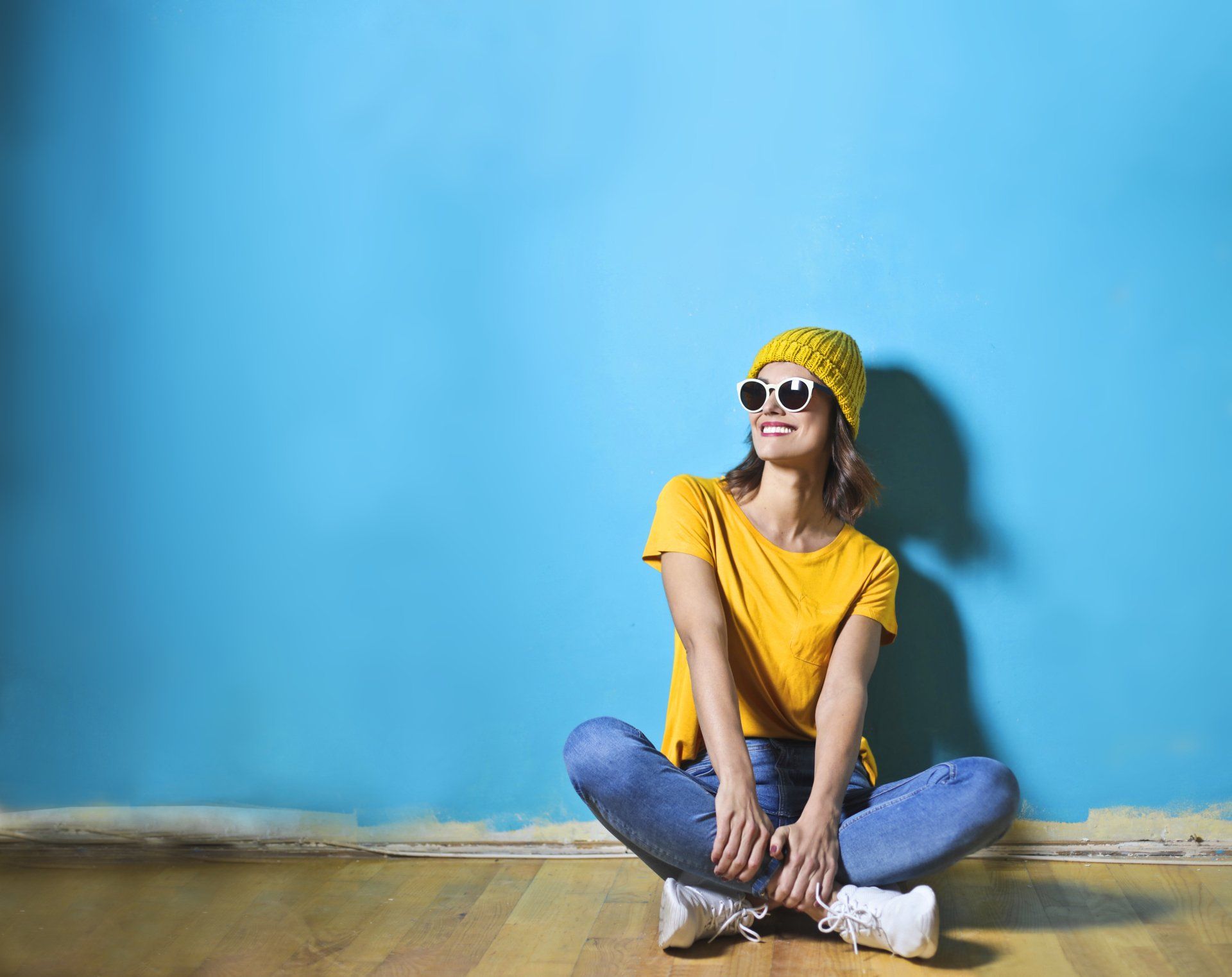 Una donna è seduta sul pavimento con le gambe incrociate contro un muro blu.