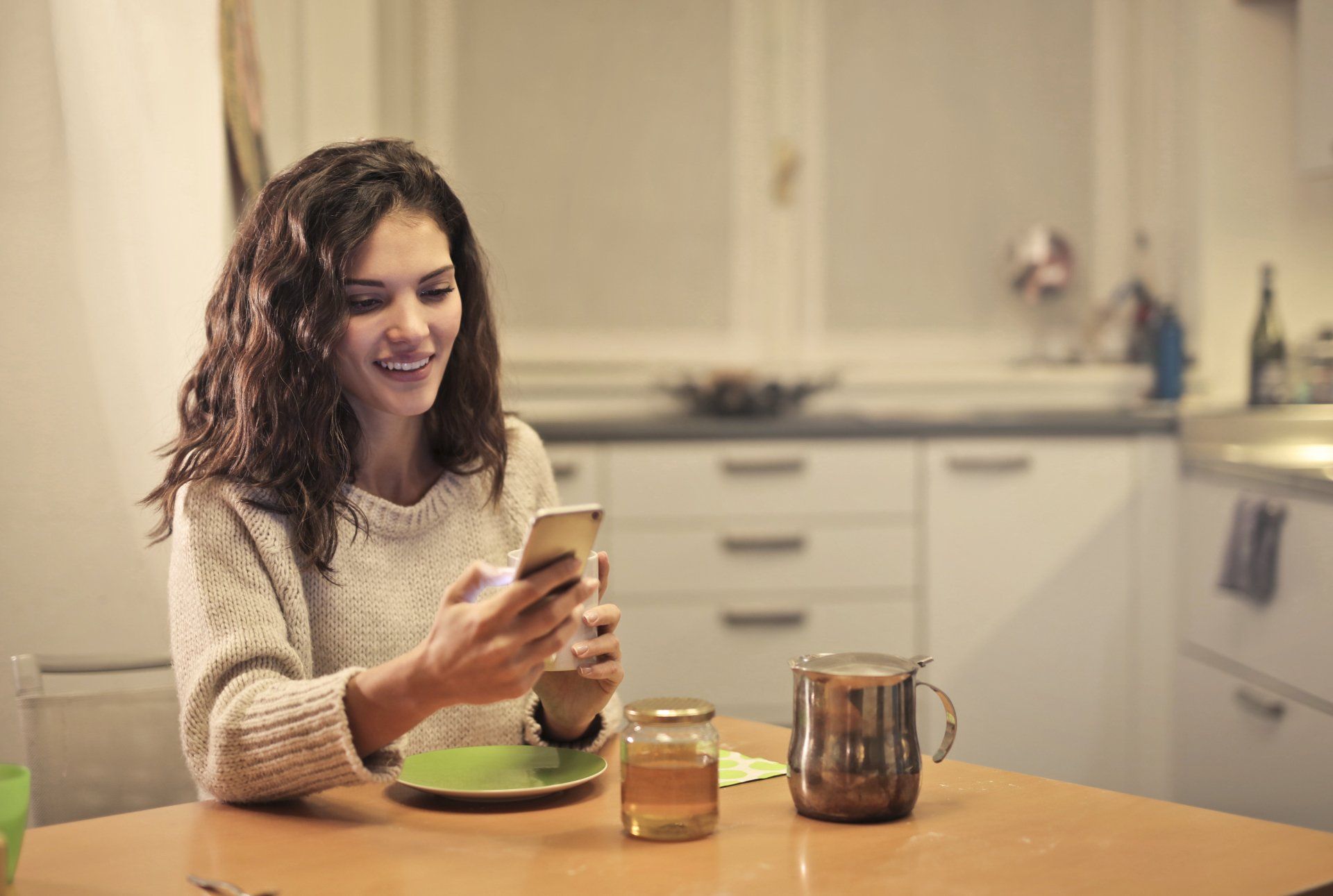 A woman is sitting at a table looking at her cell phone interacting with a chatbot.