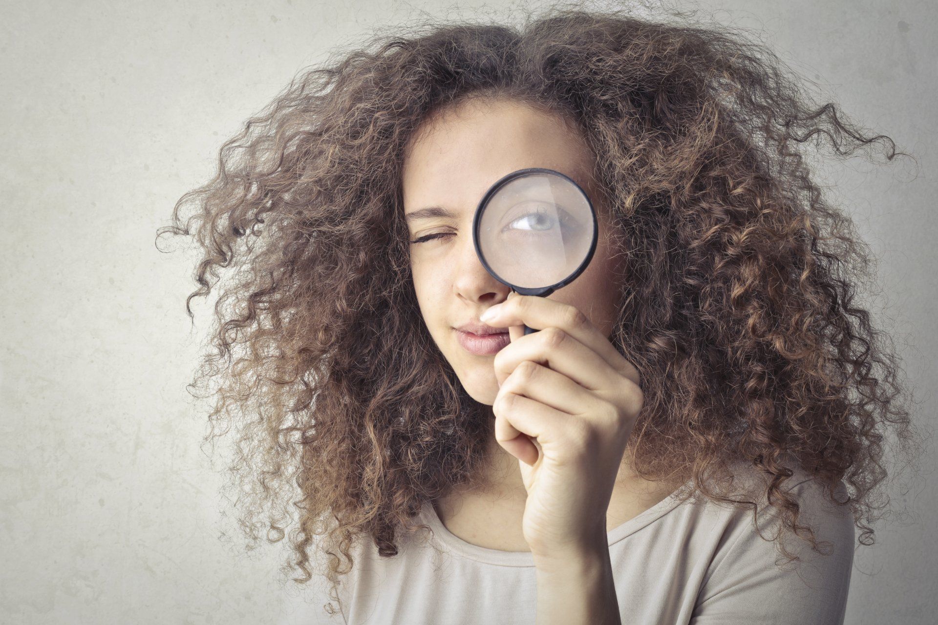 a woman with curly hair is looking through a magnifying glass .