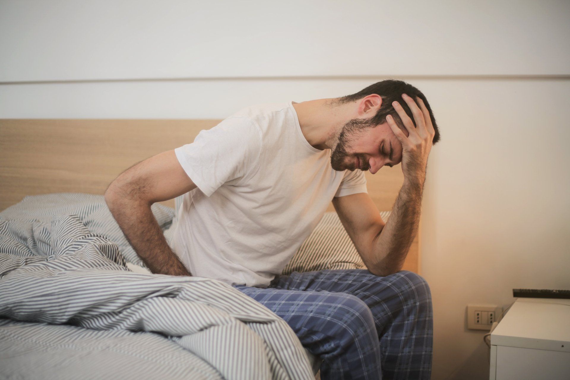 Man sitting by his bed, holding his head with visible headache.
