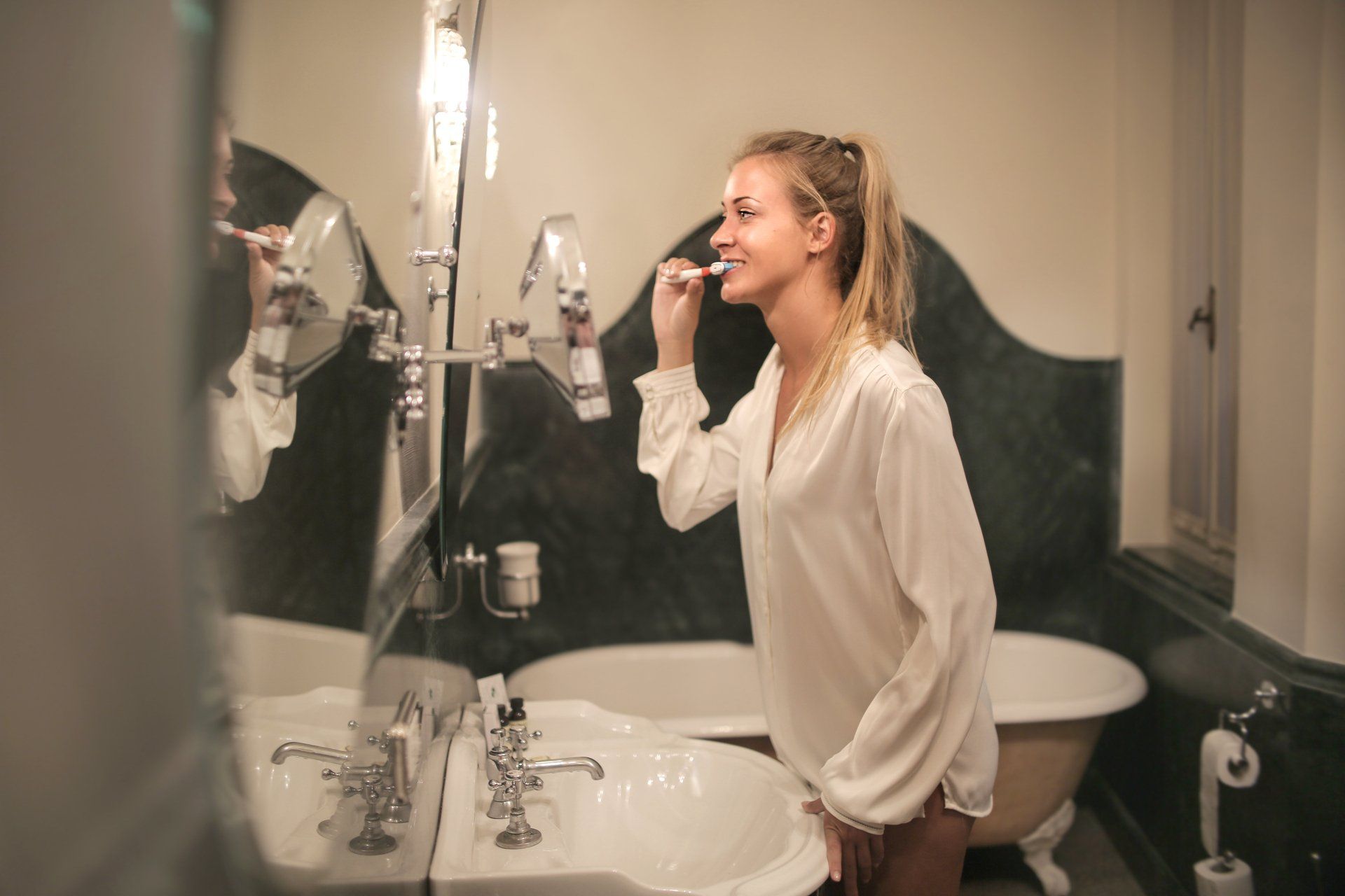 A woman is brushing her teeth in front of a mirror in a bathroom.