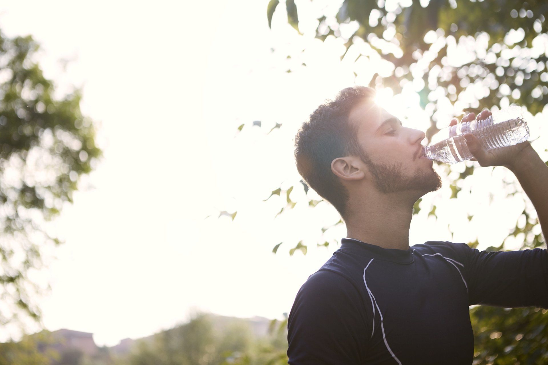 A man is drinking water from a bottle in a park.
