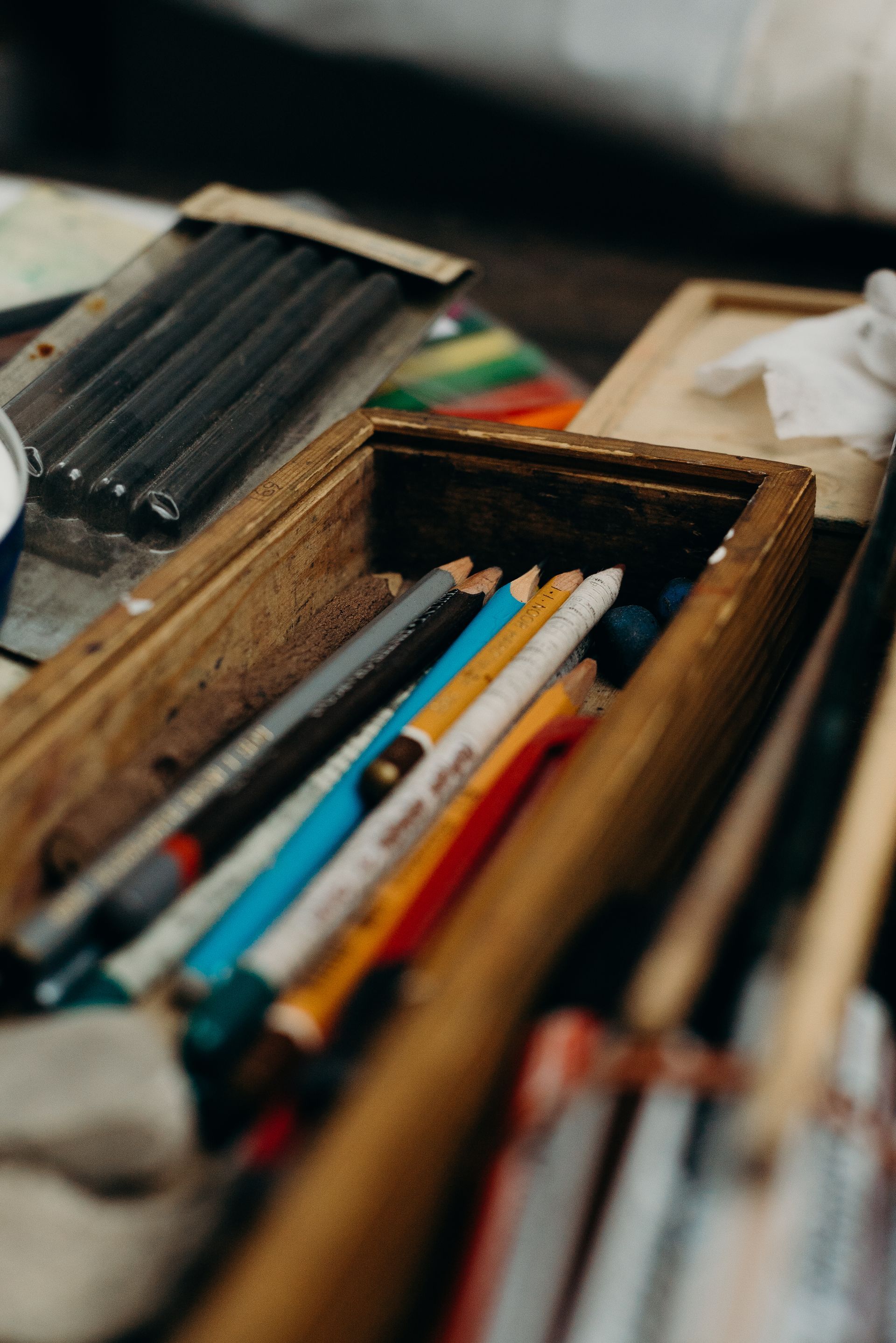 Wooden box holding colored pencils, with a package of dark pencils in the background.