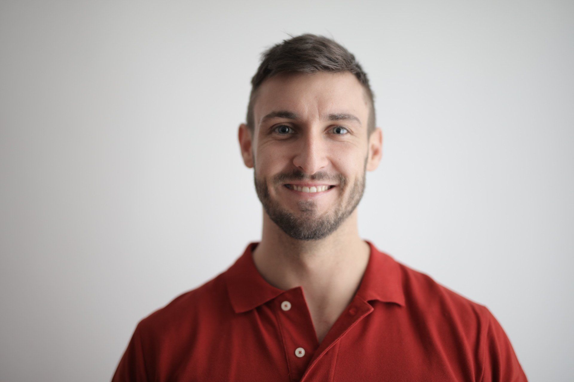 A man with a beard is wearing a red polo shirt and smiling.