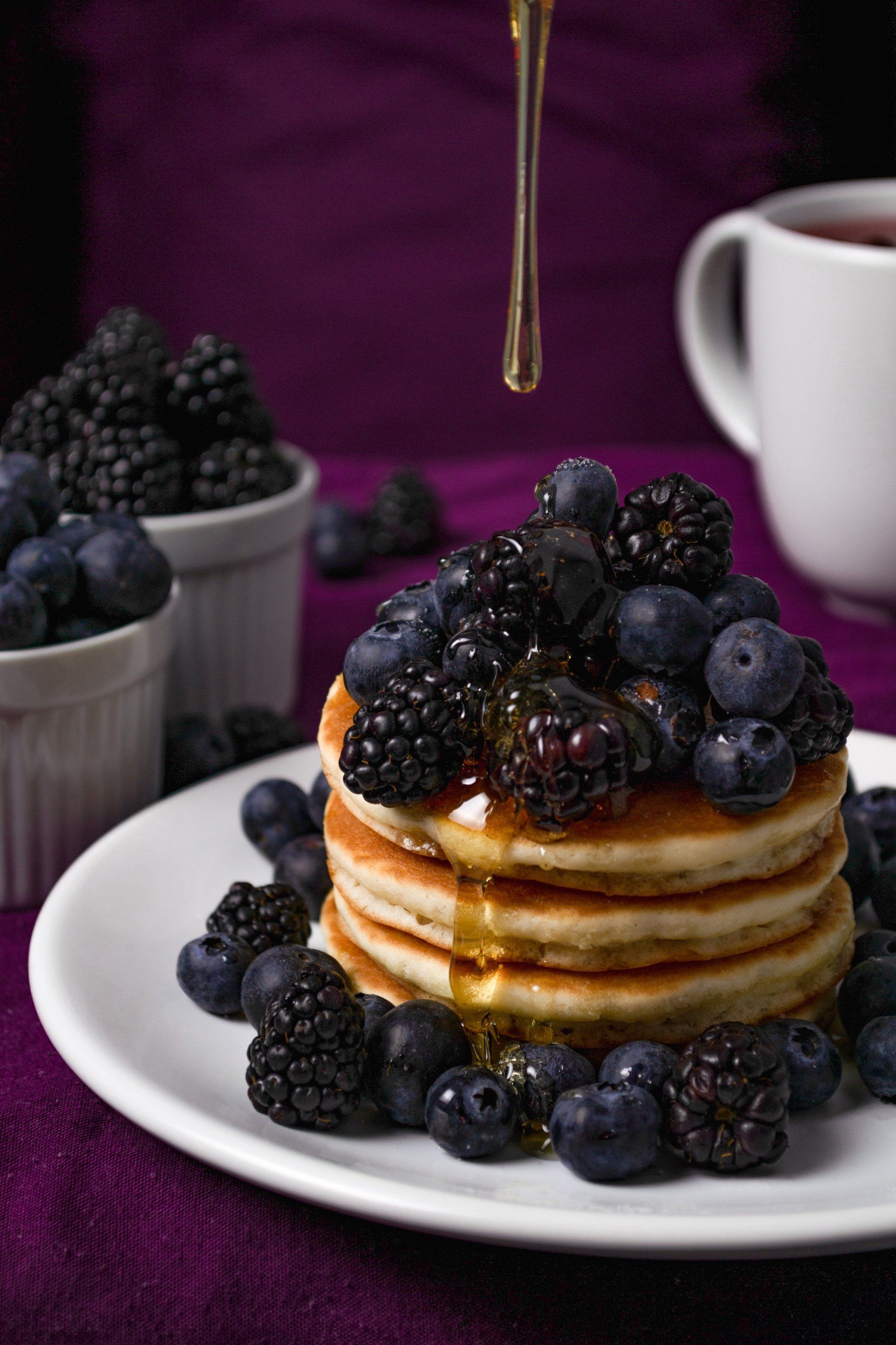 A stack of pancakes with blueberries , blackberries and syrup on a white plate.
