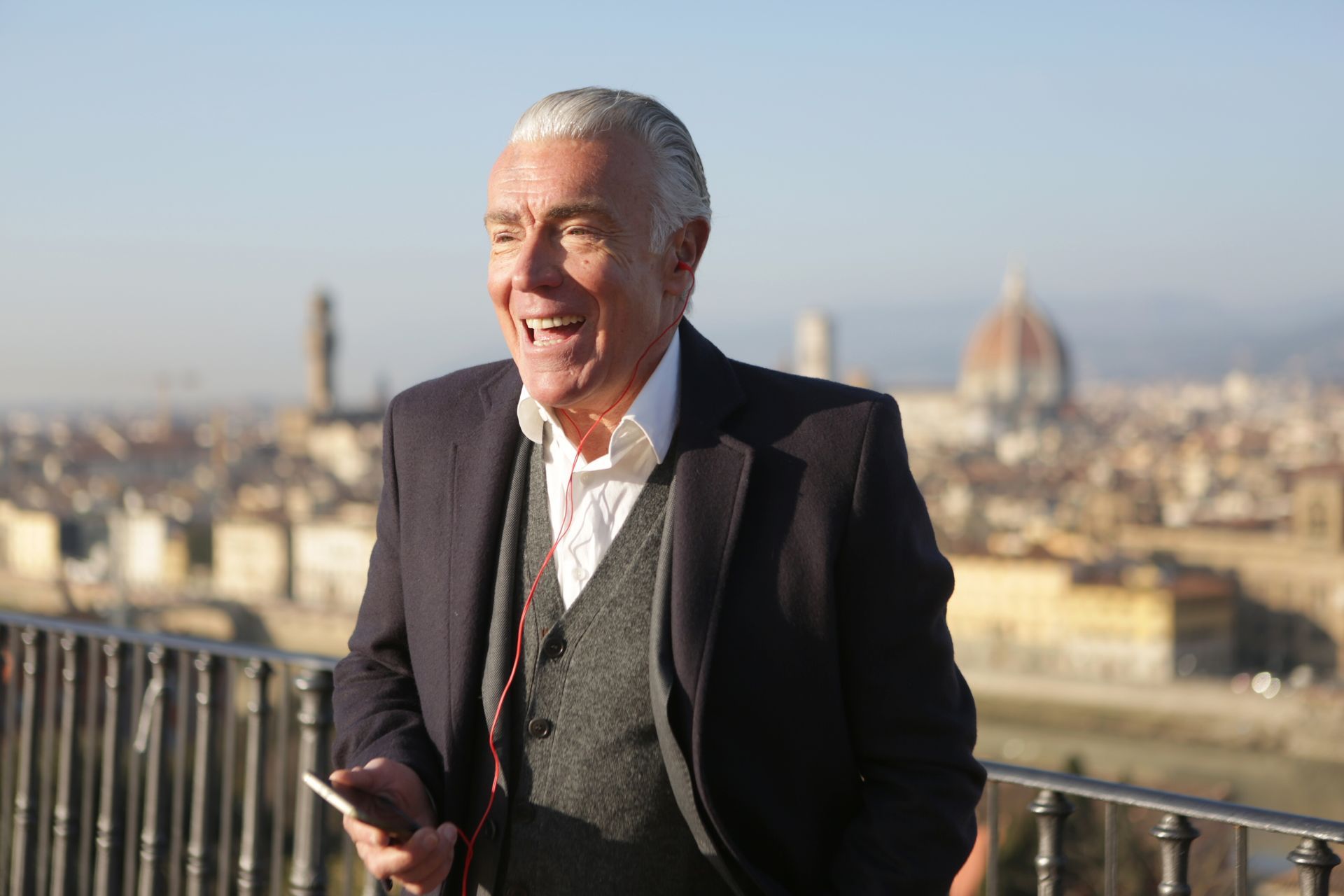 A man in a suit is standing on a balcony holding a cell phone.
