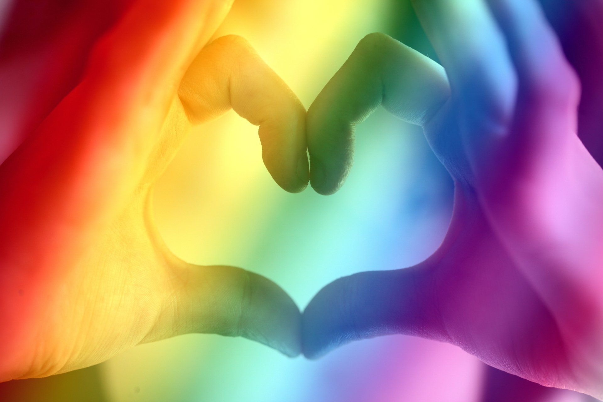 a person is making a heart shape with their hands in front of a rainbow background .