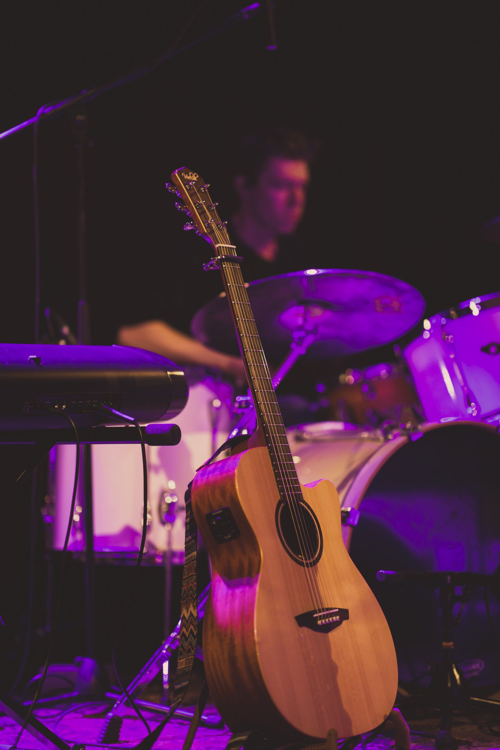 An acoustic guitar is sitting on a stage next to a drum set.