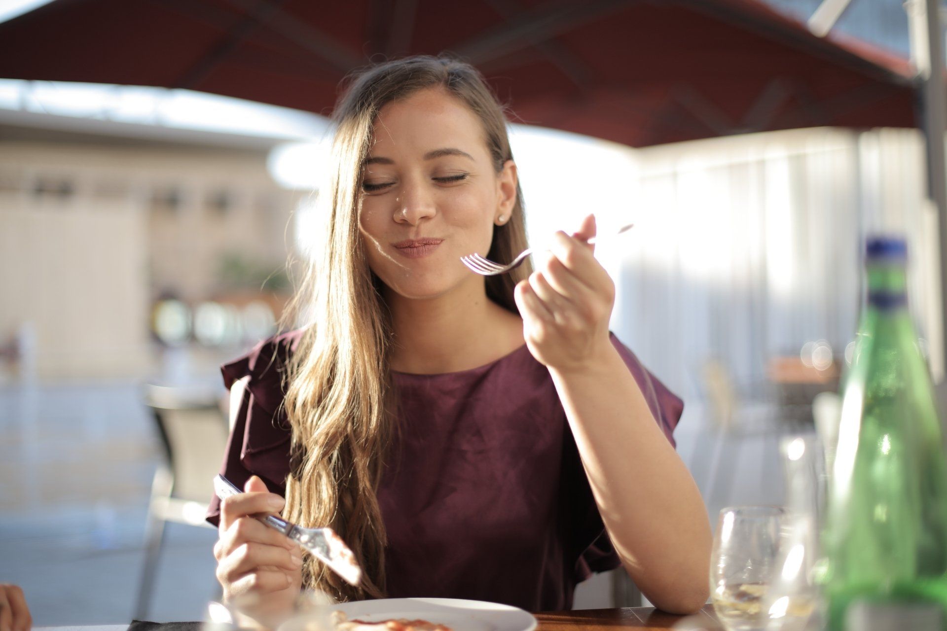 A woman is sitting at a table eating a plate of food with a fork.