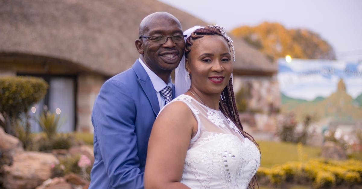 A bride and groom are posing for a picture in front of a thatched building.