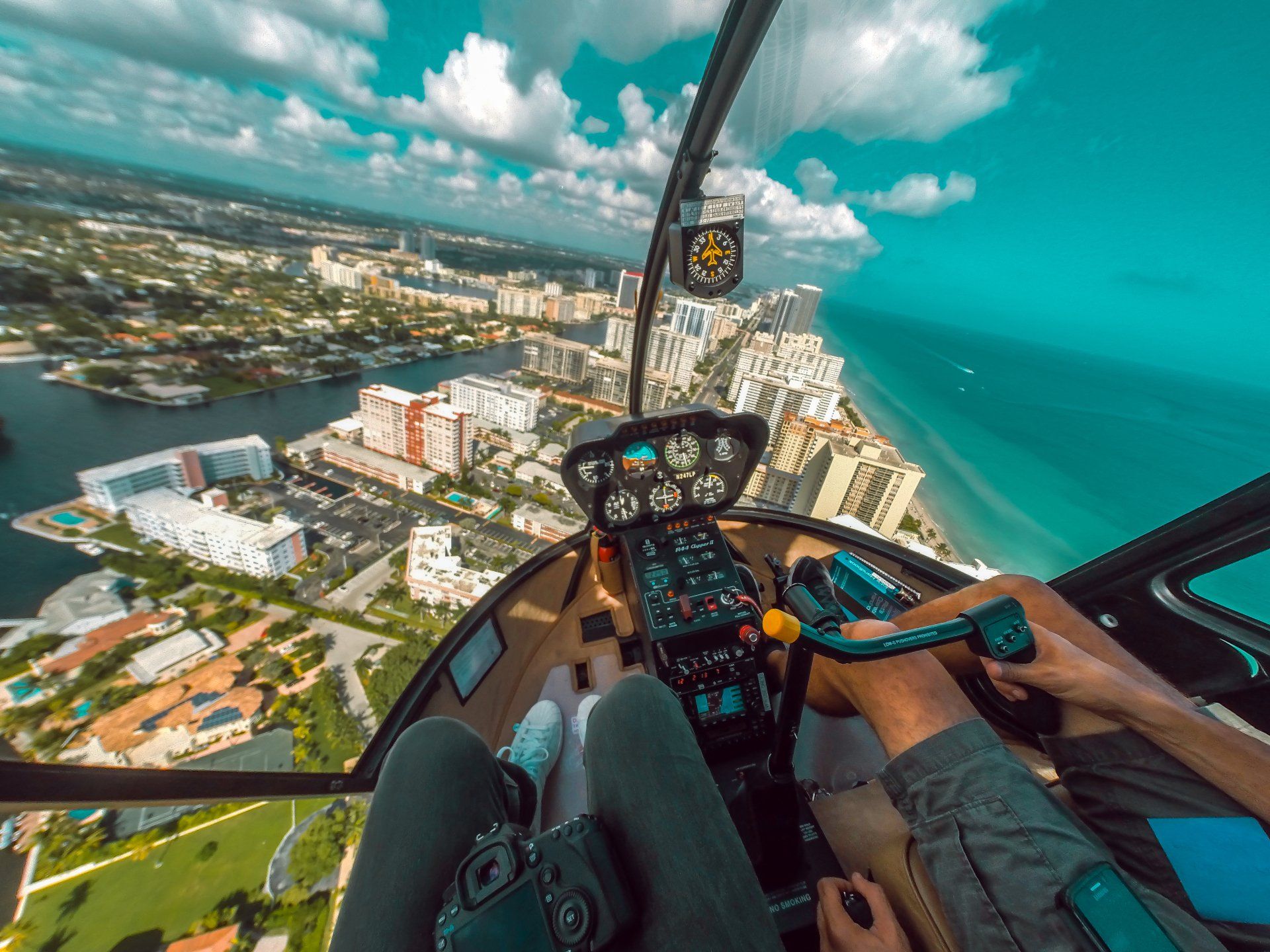 A person is sitting in the cockpit of a helicopter over a city.