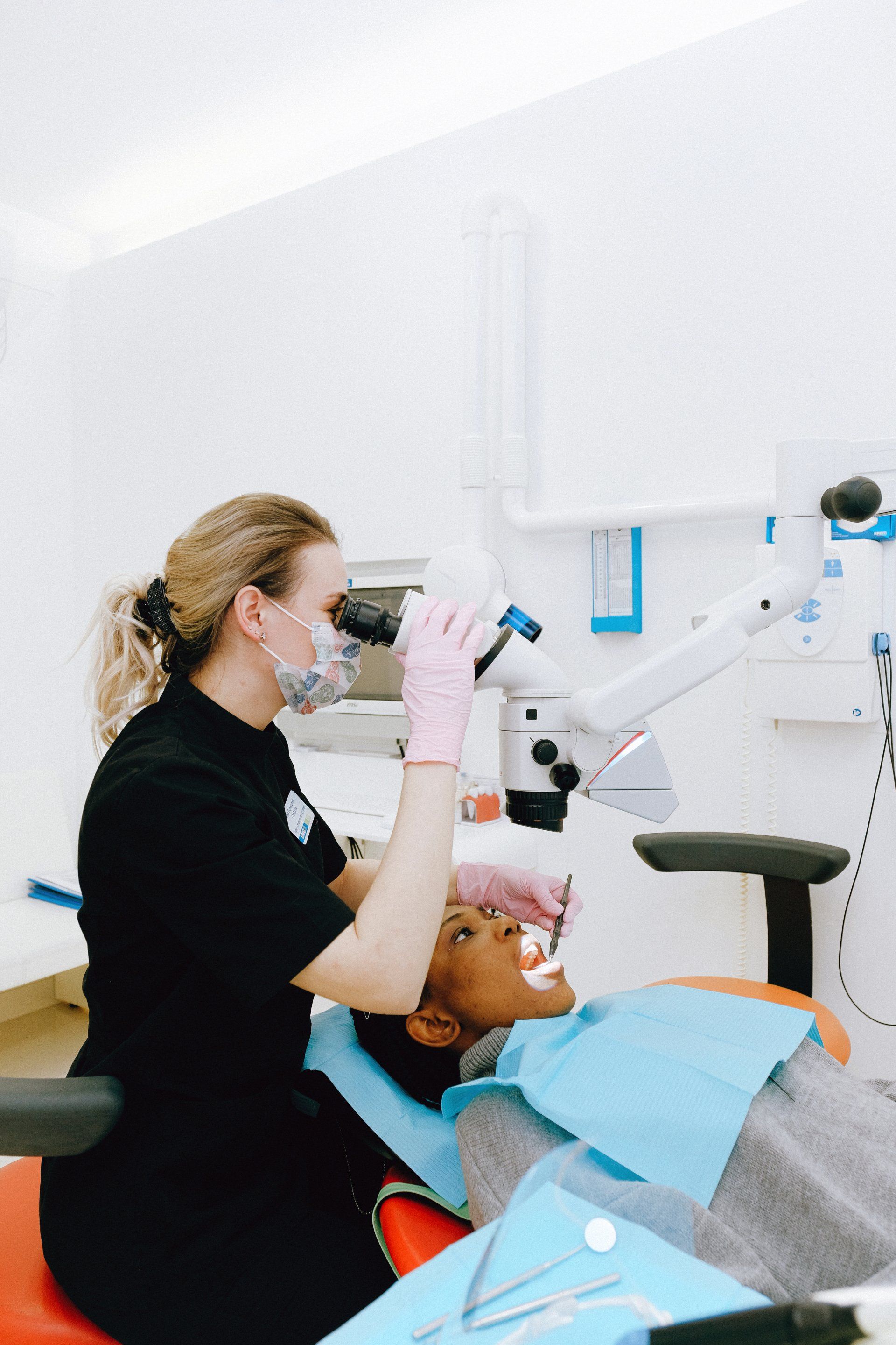 A dentist is looking through a microscope at a patient 's teeth.