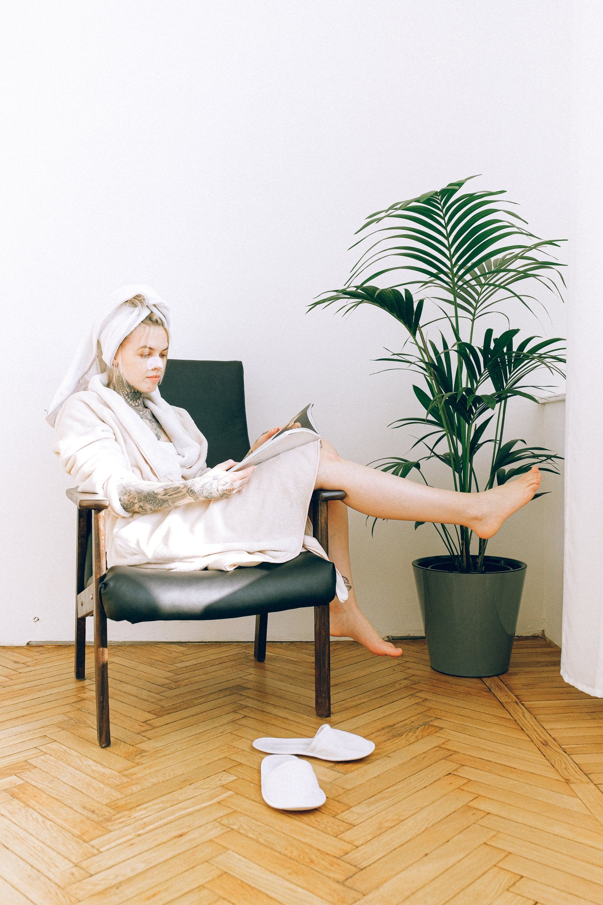 A woman in a bathrobe is sitting in a chair reading a magazine.