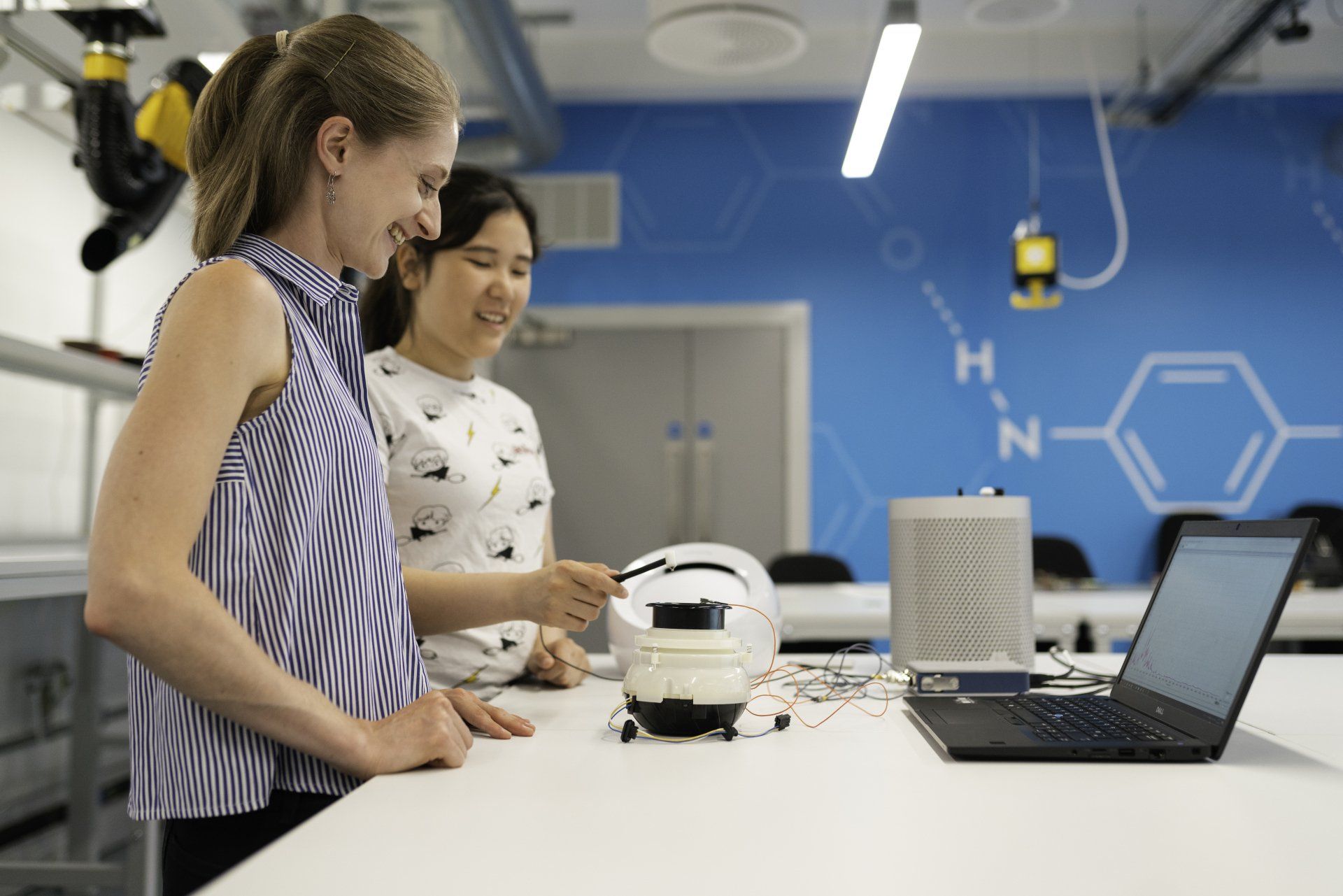 Two women are standing next to each other in a lab looking at a robot.