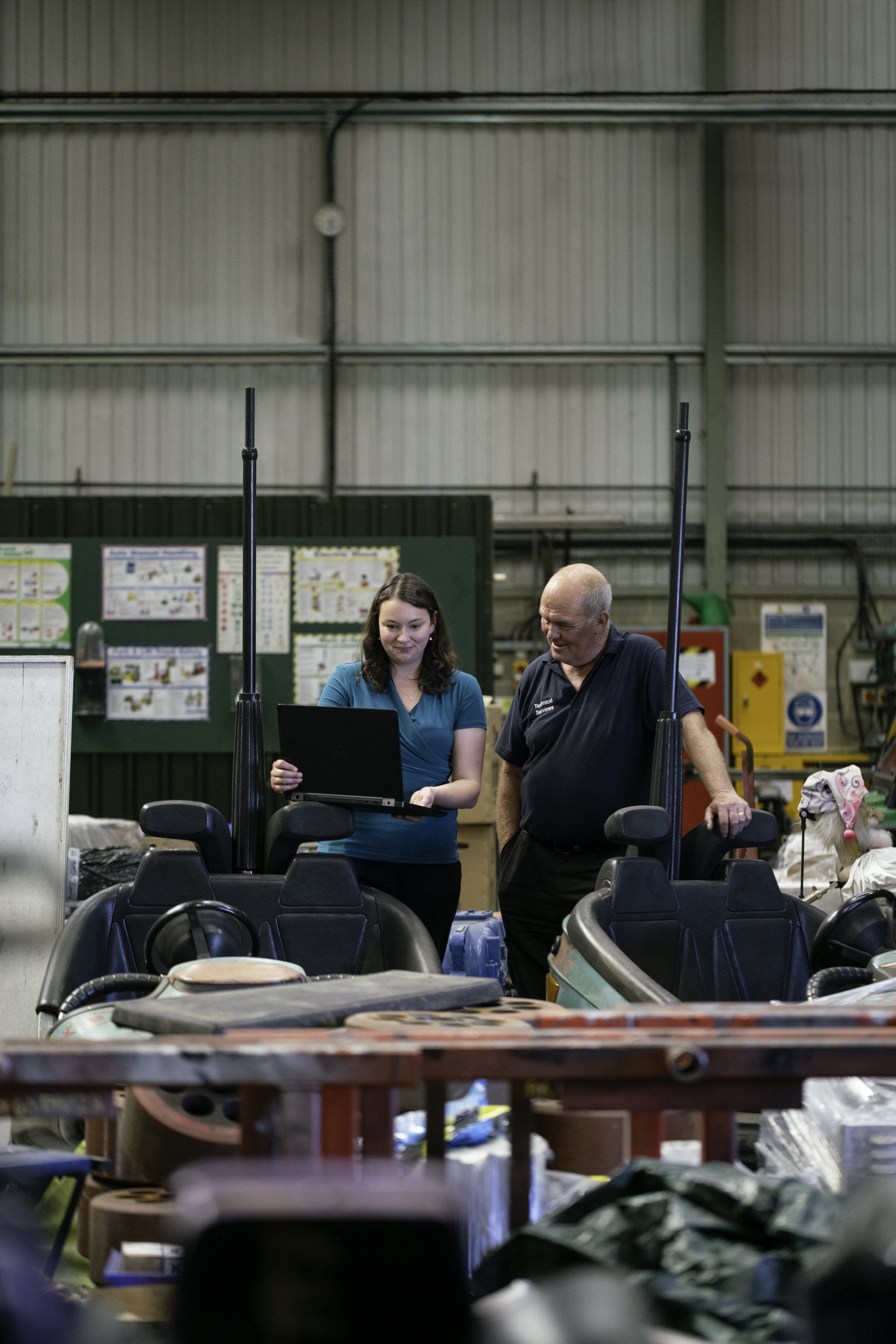 A man and a woman are standing in a warehouse looking at a laptop.