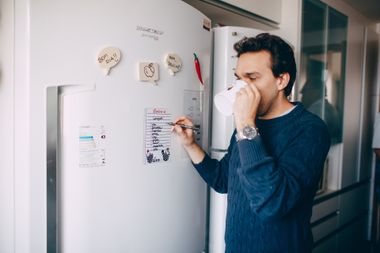 A man is drinking a cup of coffee in front of a refrigerator.