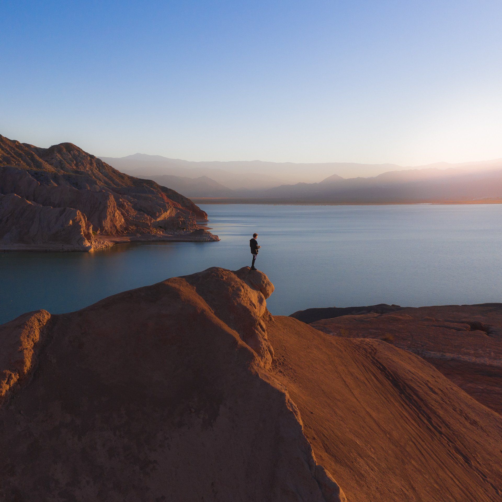 A person standing on top of a hill overlooking a lake