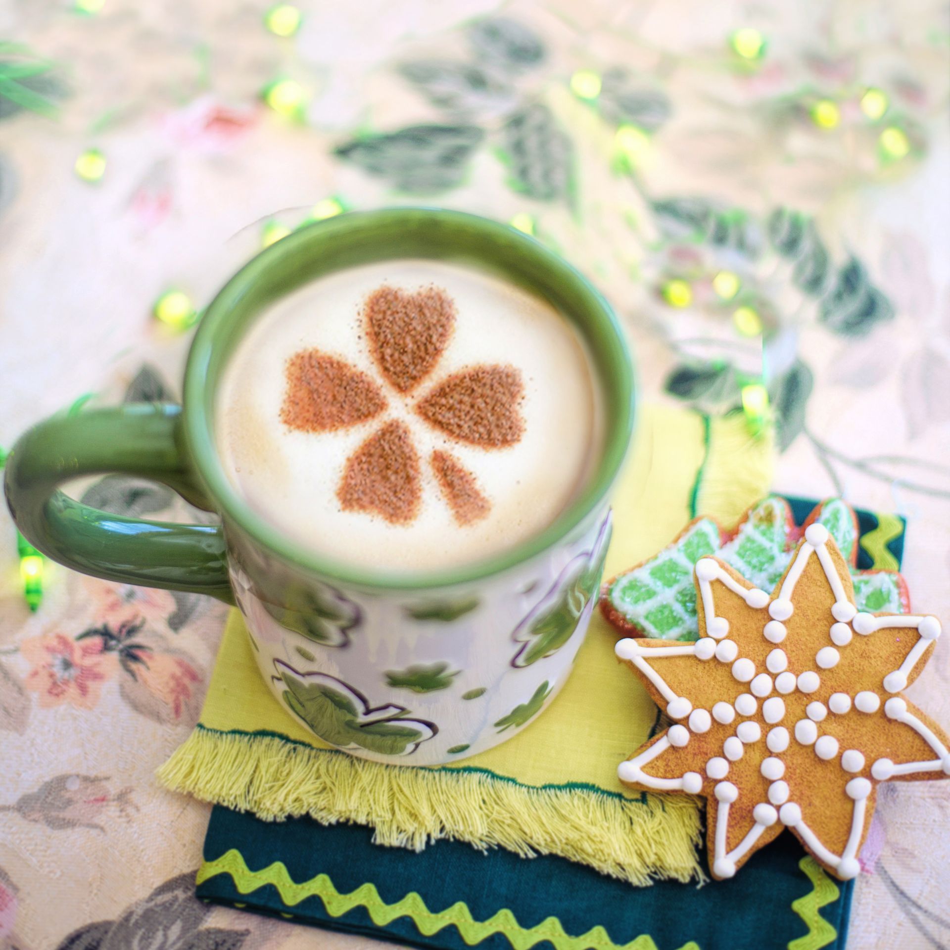 a cup of coffee with a flower design on the foam next to a gingerbread cookie