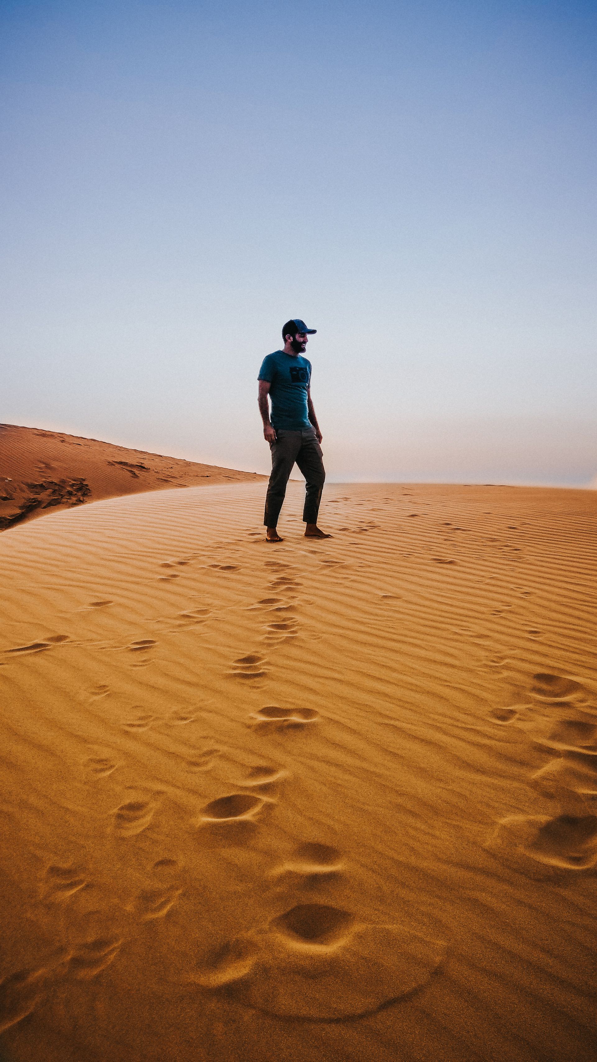 A man is standing on top of a sand dune in the desert.