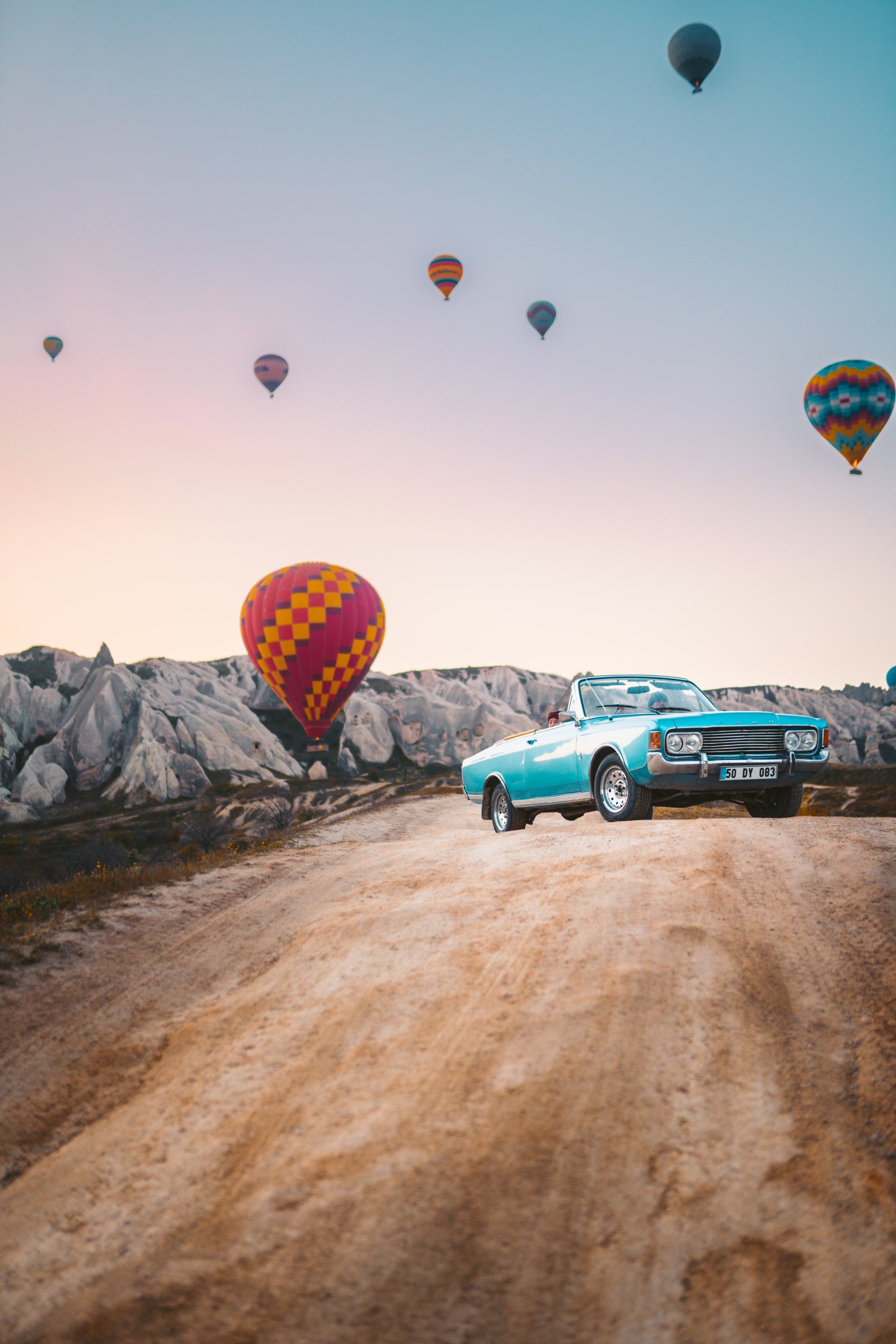 a car is driving down a dirt road with hot air balloons in the background .