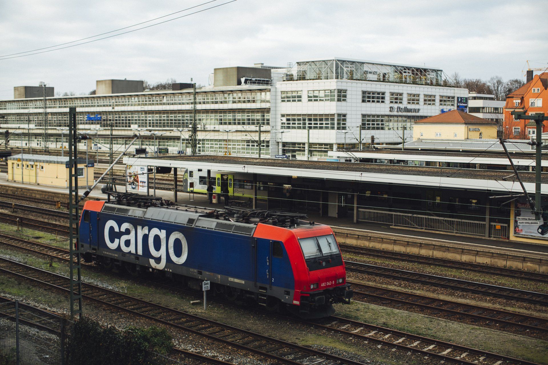 A cargo train is sitting on the tracks at a train station.