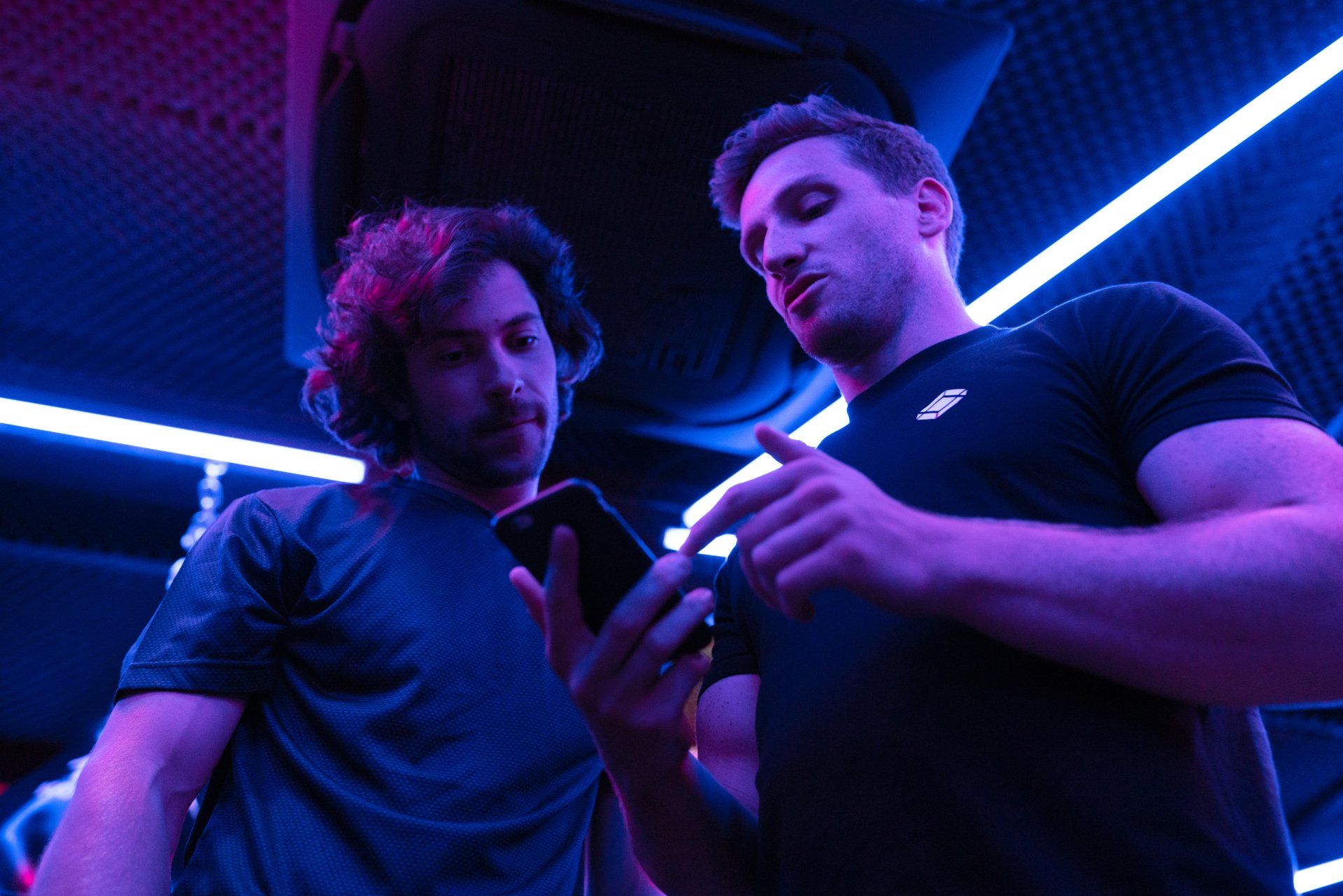 Zwei Männer schauen in einem dunklen Raum auf ein Handy.