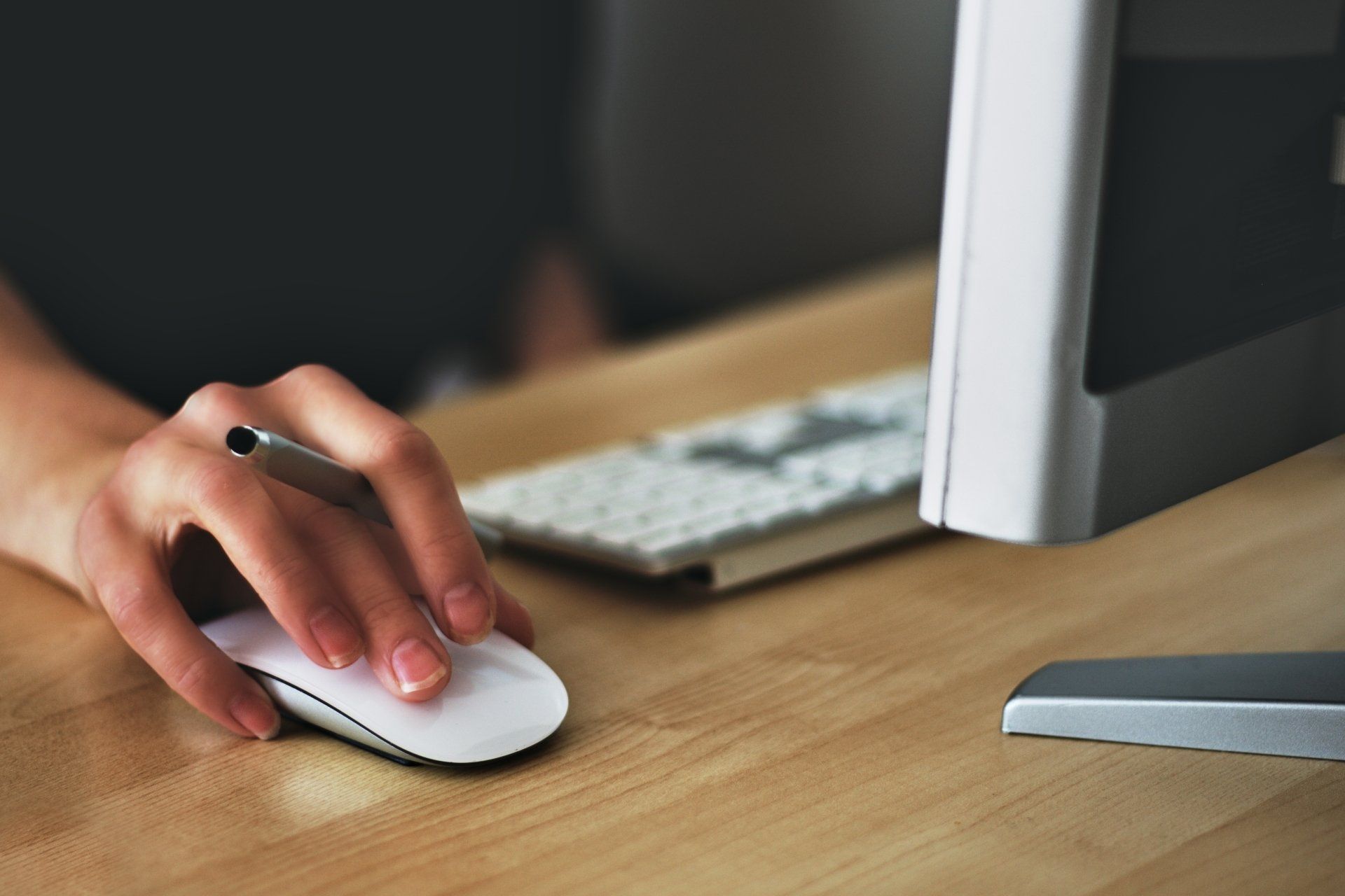 Photo of a hand on a computer mouse, with a computer monitor and keyboard in the frame