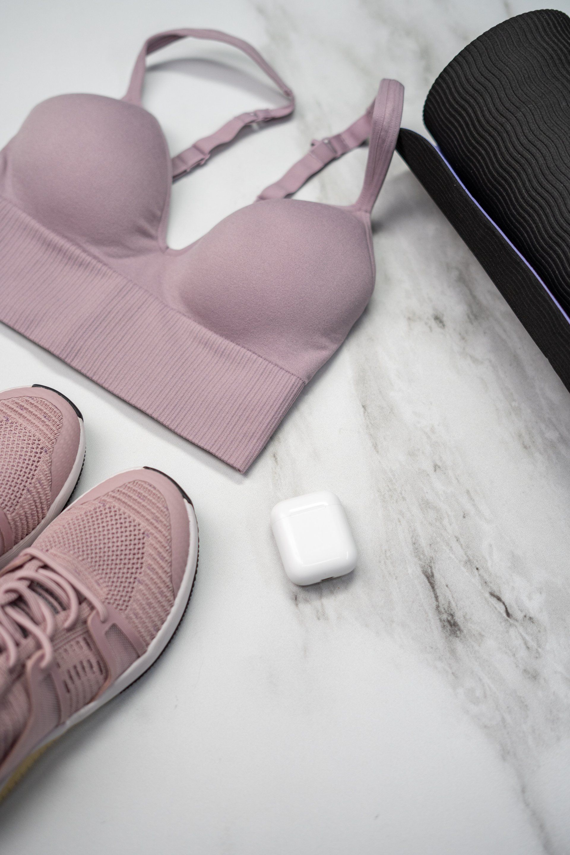 A pink sports bra , pink sneakers , and a yoga mat on a marble surface.