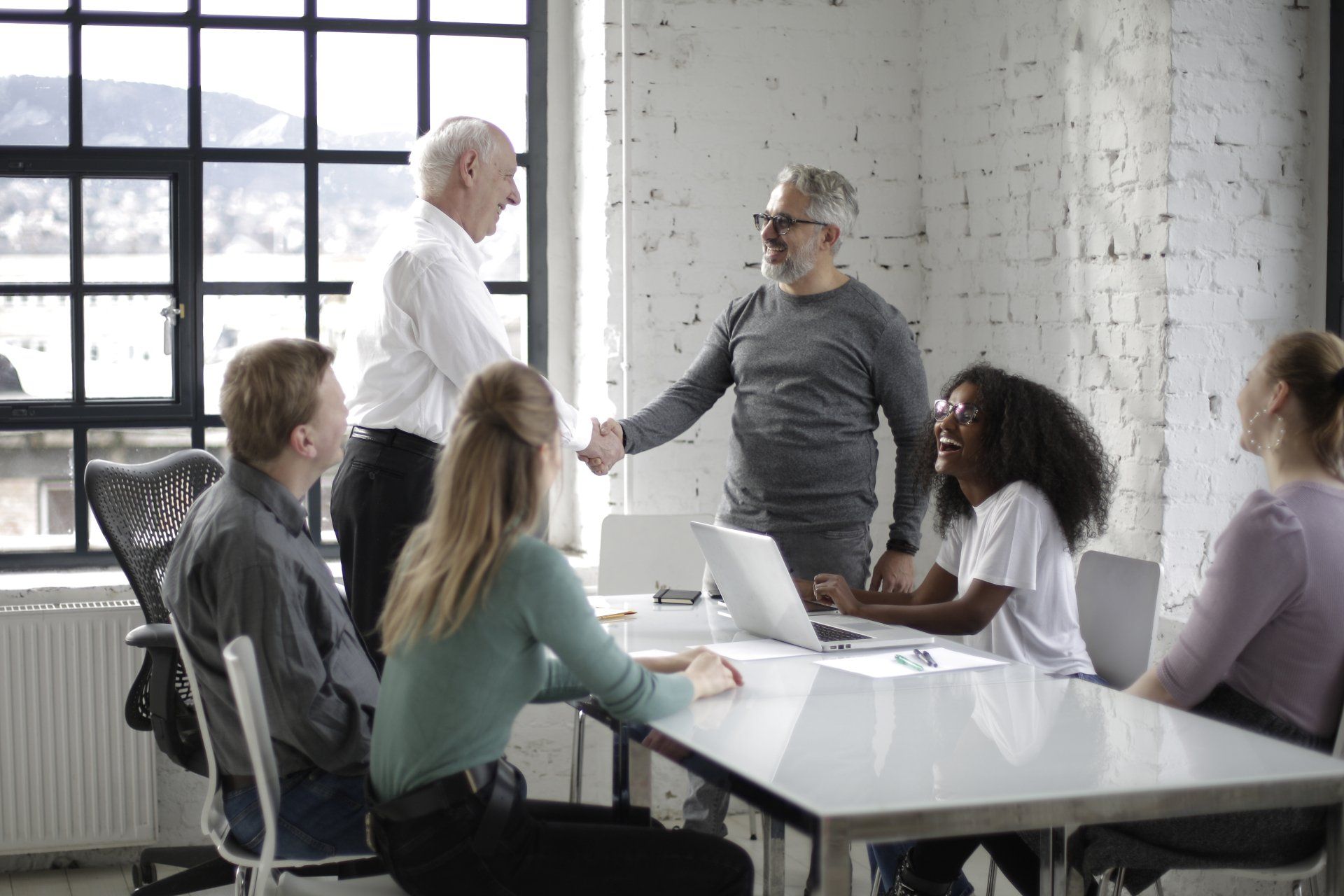 A group of people are sitting around a table shaking hands.