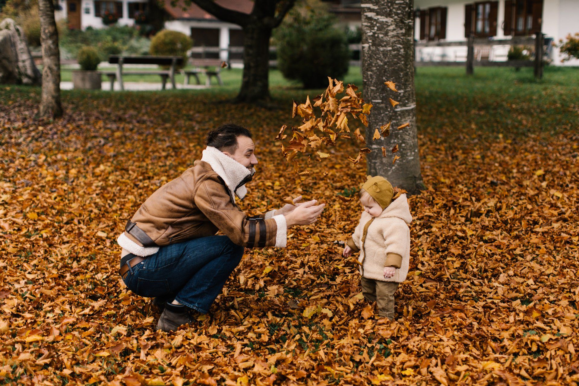 A man and a child are playing with leaves in a park.