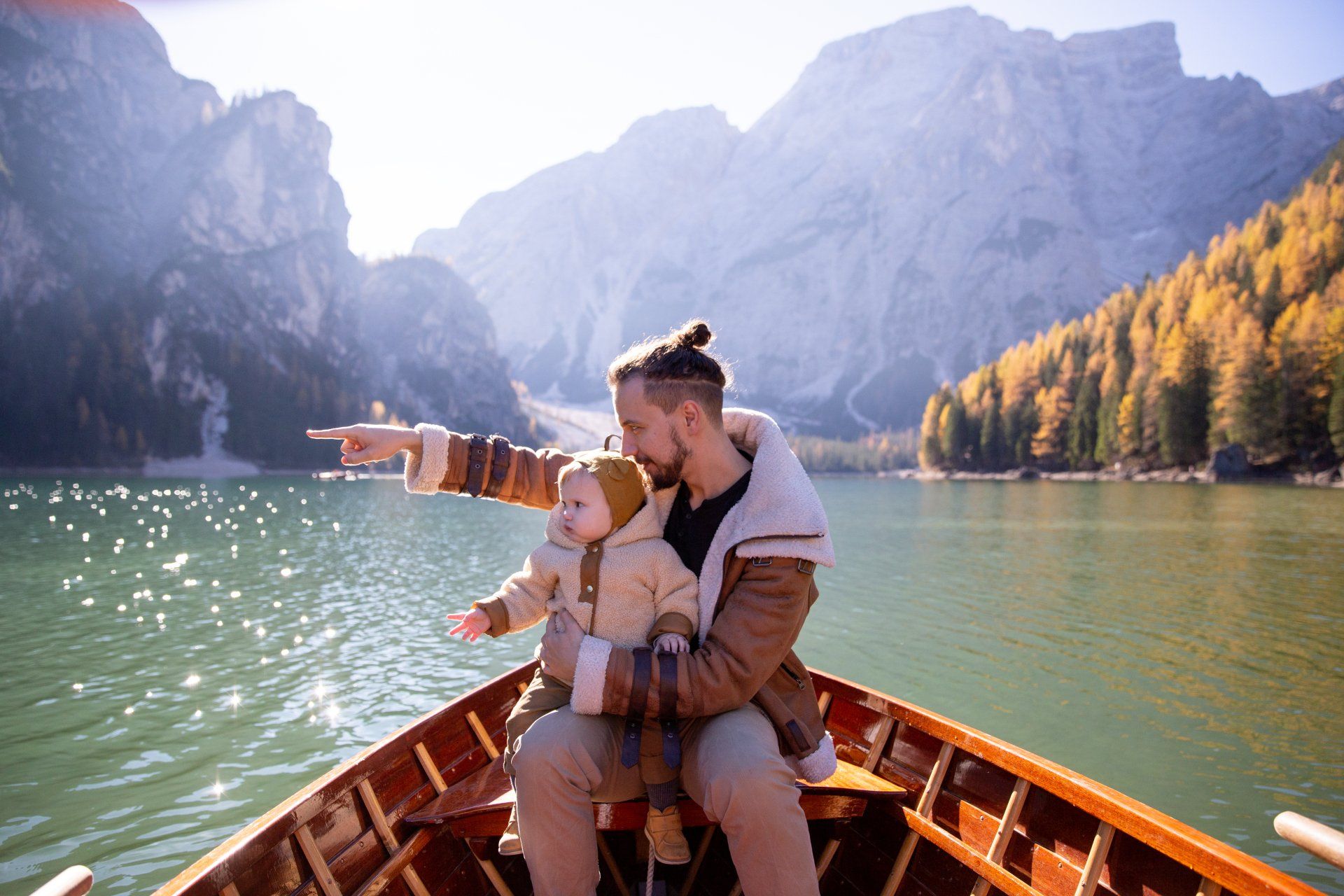A man is holding a baby while sitting in a boat on a lake.