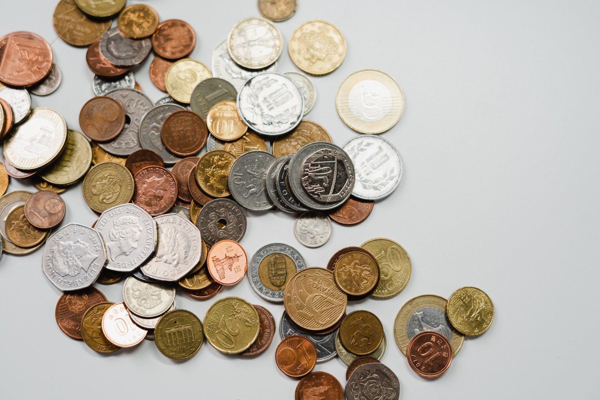 Scattered coins of various sizes and colors on a gray surface.