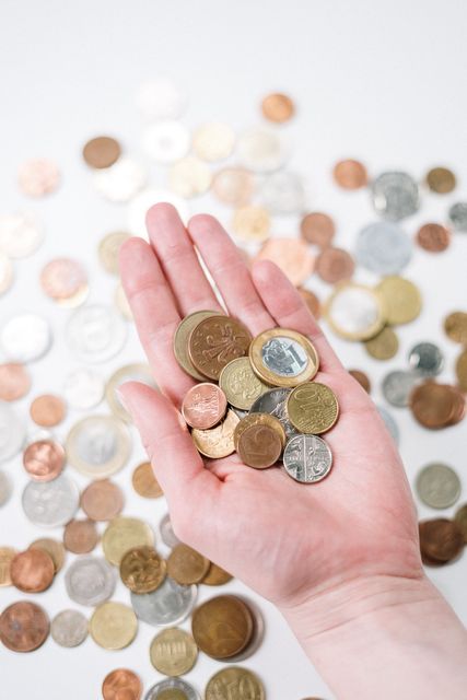 Hand holding a variety of coins, with more scattered on a white surface.