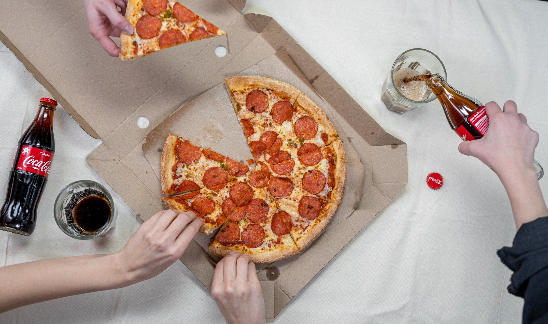 A person is taking a slice of pepperoni pizza from a box.
