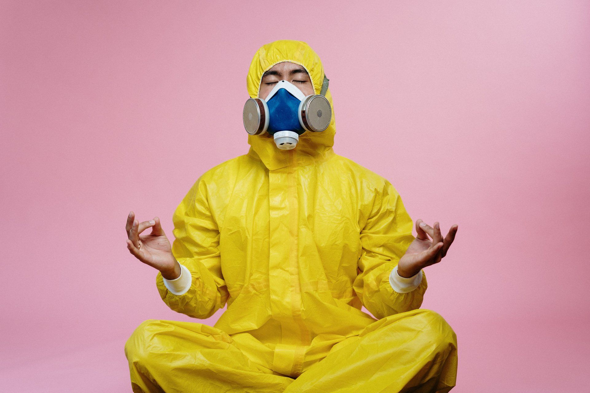 A man in a yellow protective suit and gas mask is sitting in a lotus position.