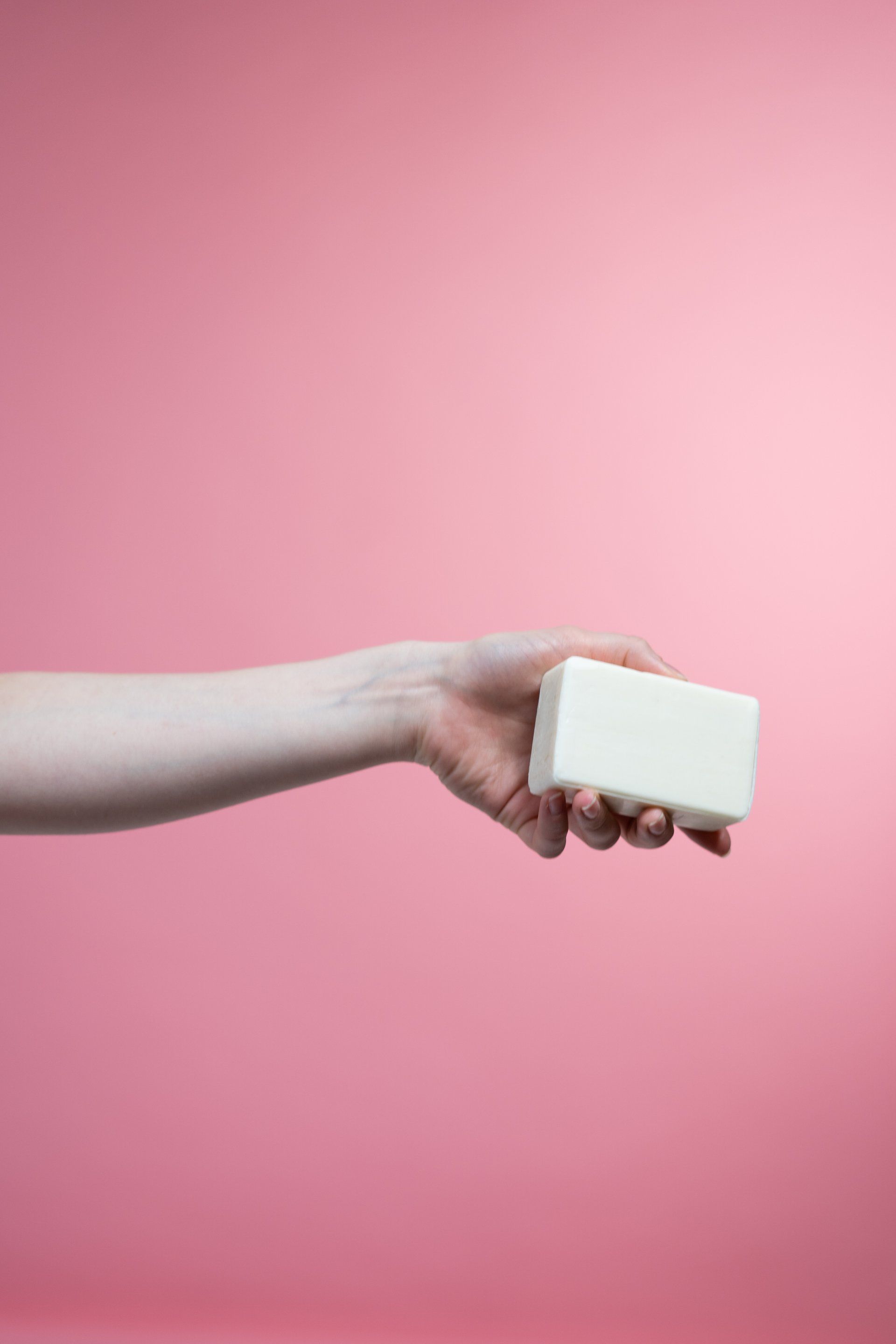 a hand is holding a white bar of soap on a pink background .