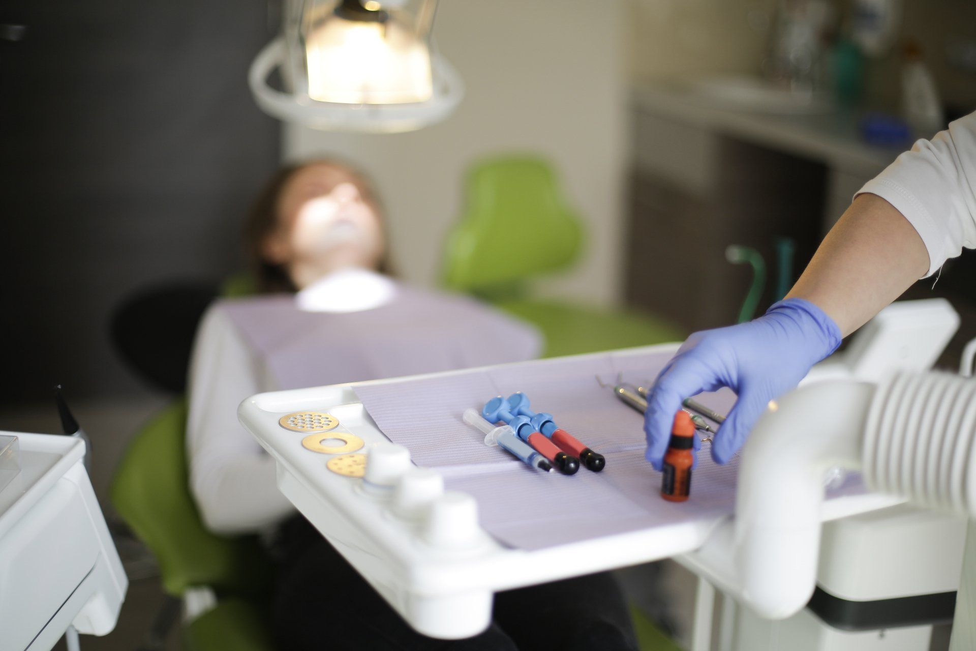 A woman is laying in a dental chair while a dentist holds a tray of tools.
