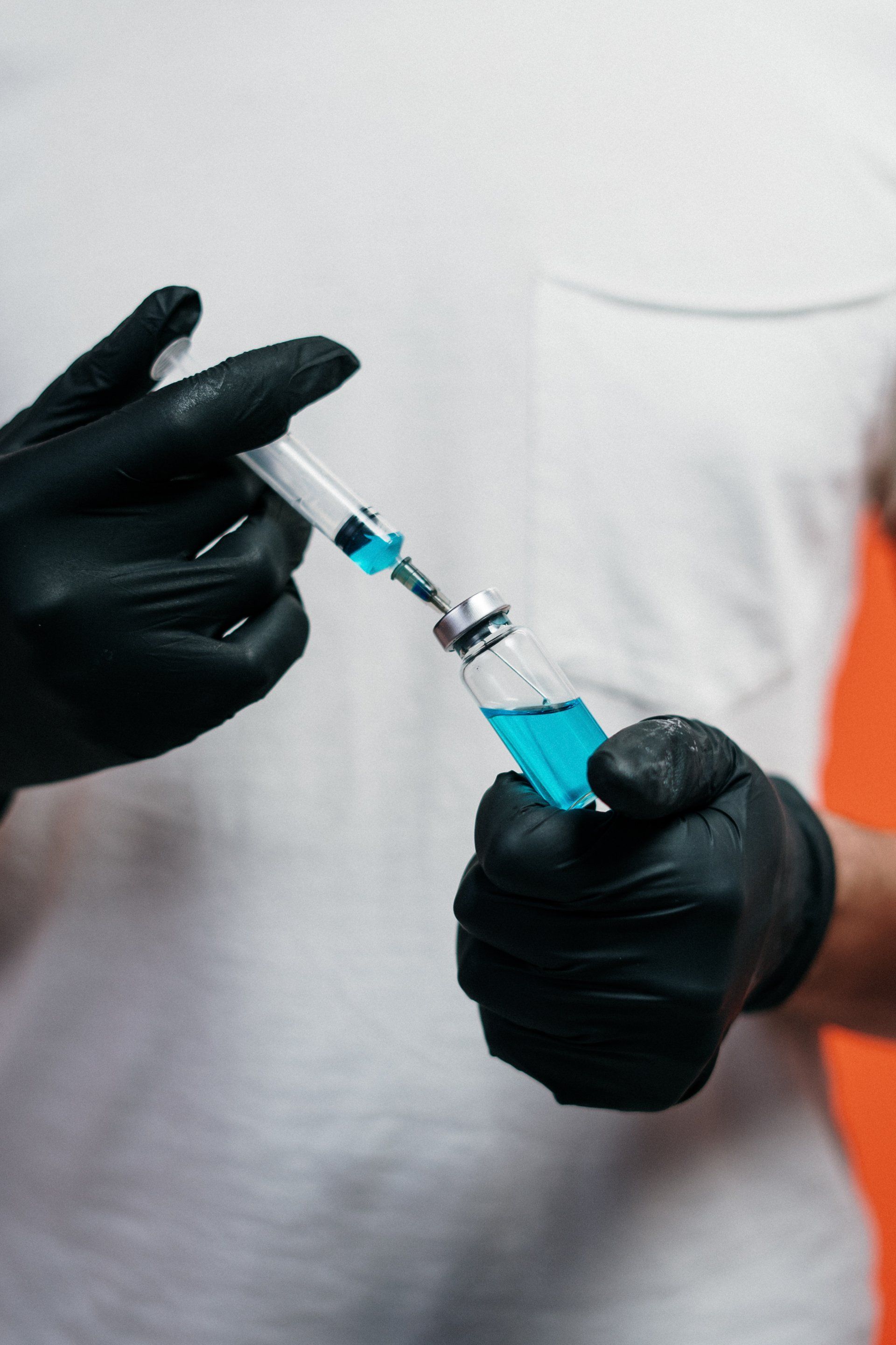 A person wearing black gloves is holding a syringe and a bottle of blue liquid.