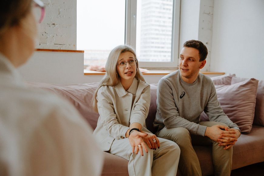 A man and a woman are sitting on a couch talking to a woman.