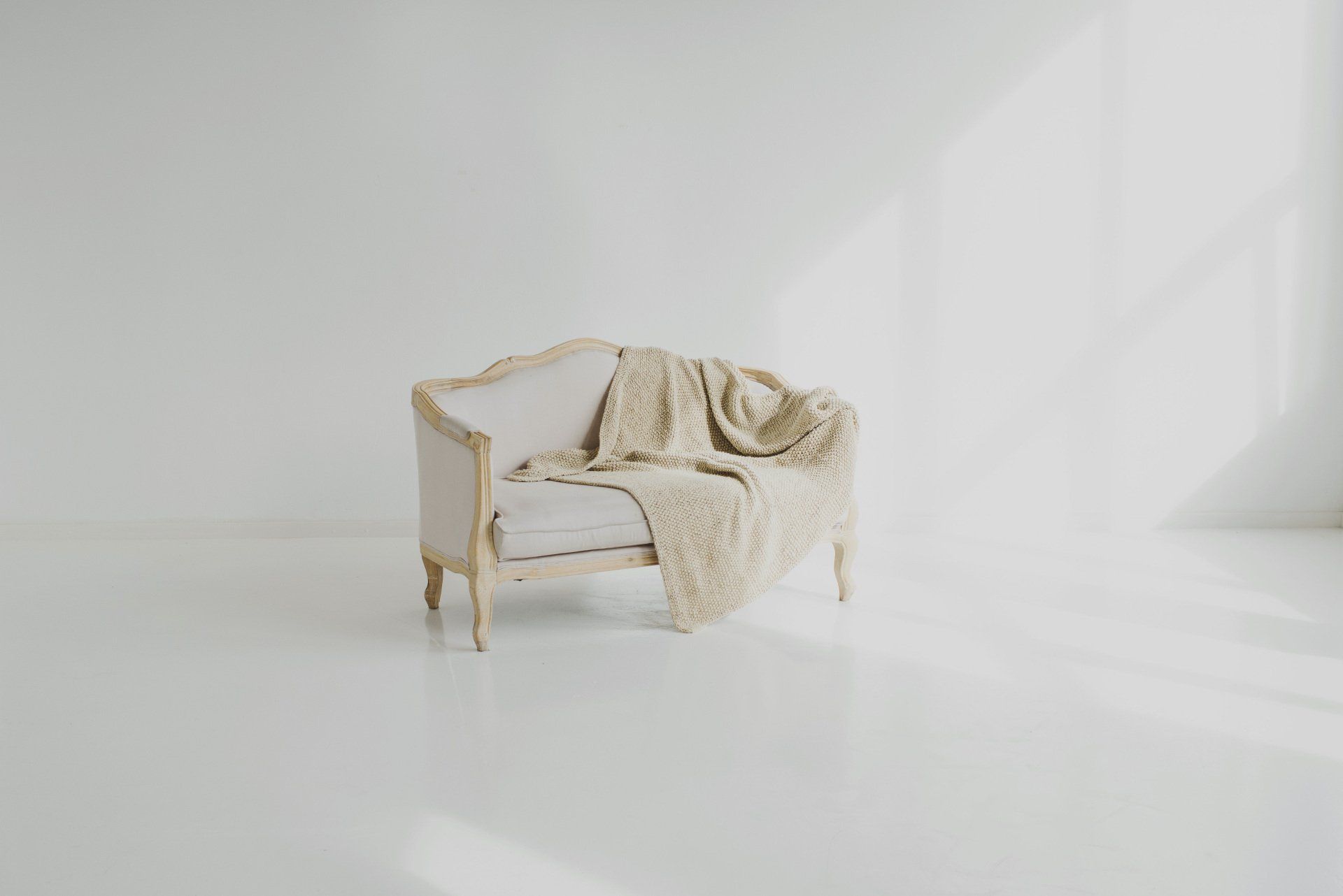 A white couch with a blanket on it in a white room.