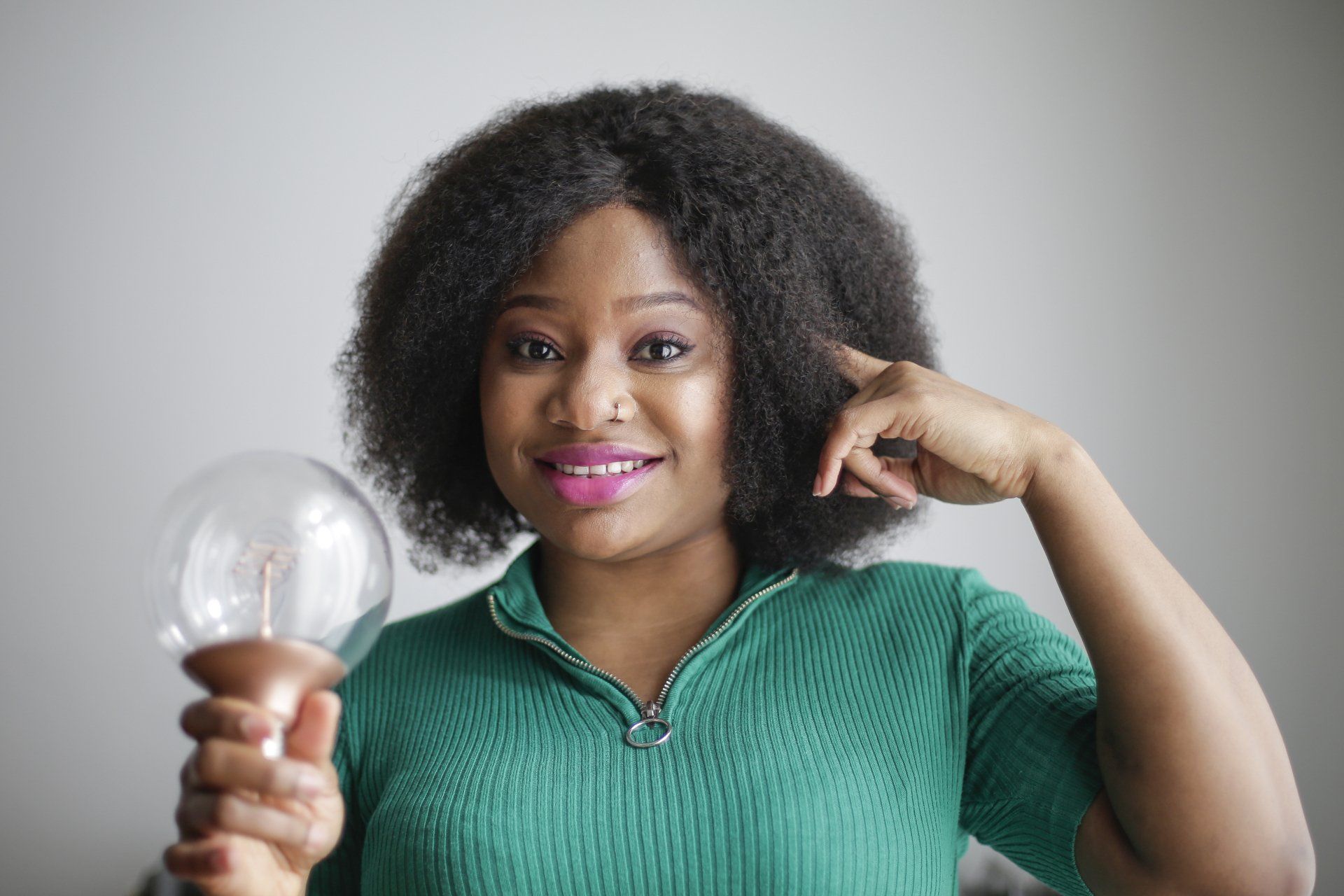 a woman in a green shirt is holding a light bulb in her hand representing ideas pointing to her brain as she gets ideas from Brainspotting and using Bilateral music
