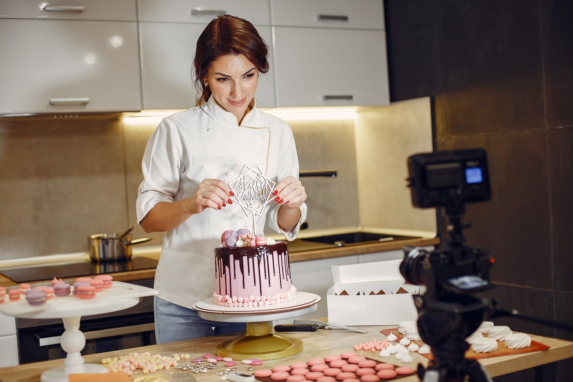 A woman is decorating a cake in front of a camera in a kitchen.