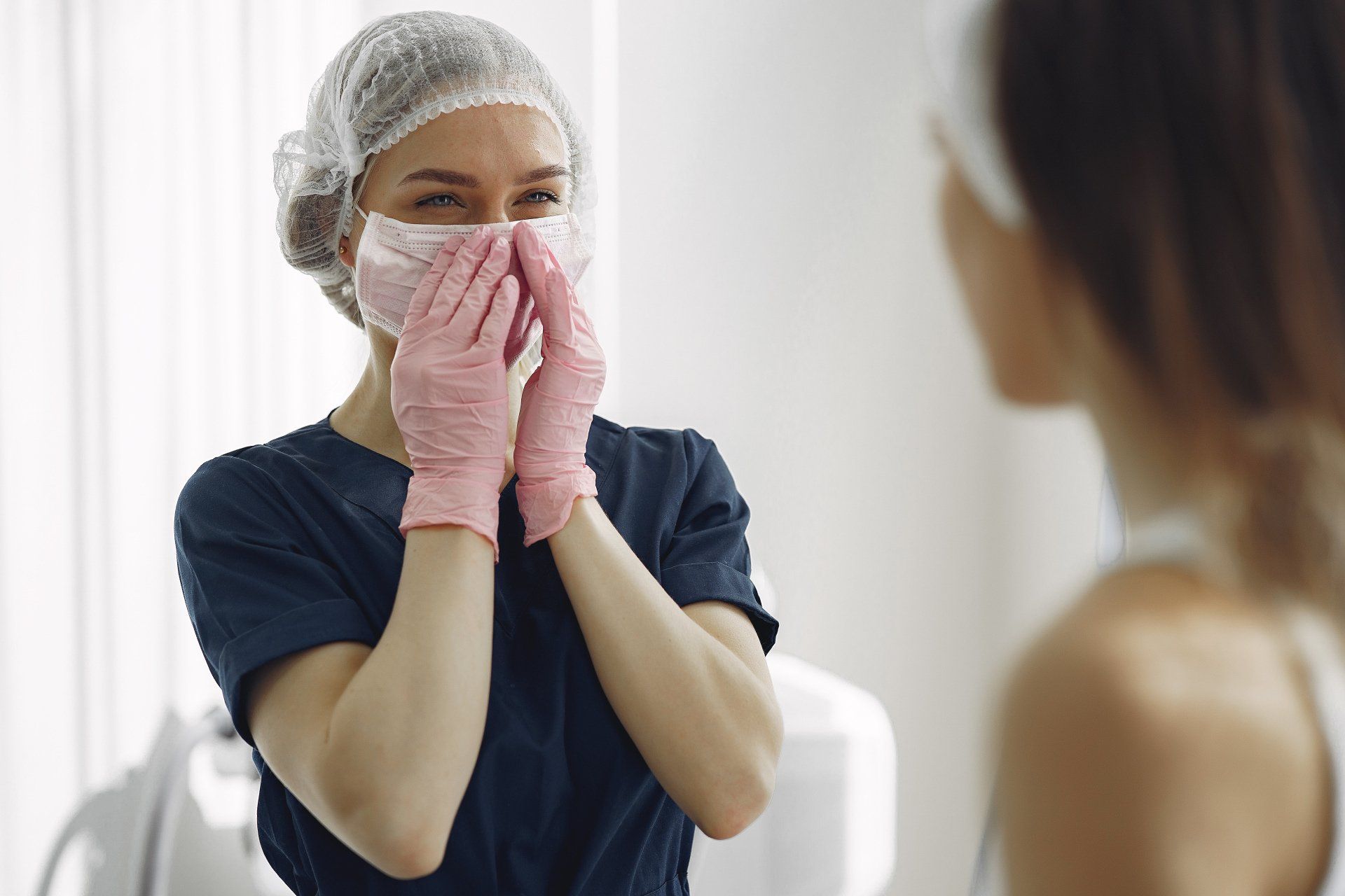 A woman wearing a mask and pink gloves is looking at herself in the mirror.