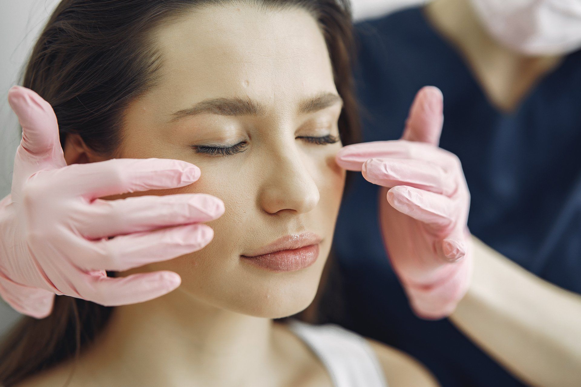 A woman is getting a facial treatment from a doctor wearing pink gloves.